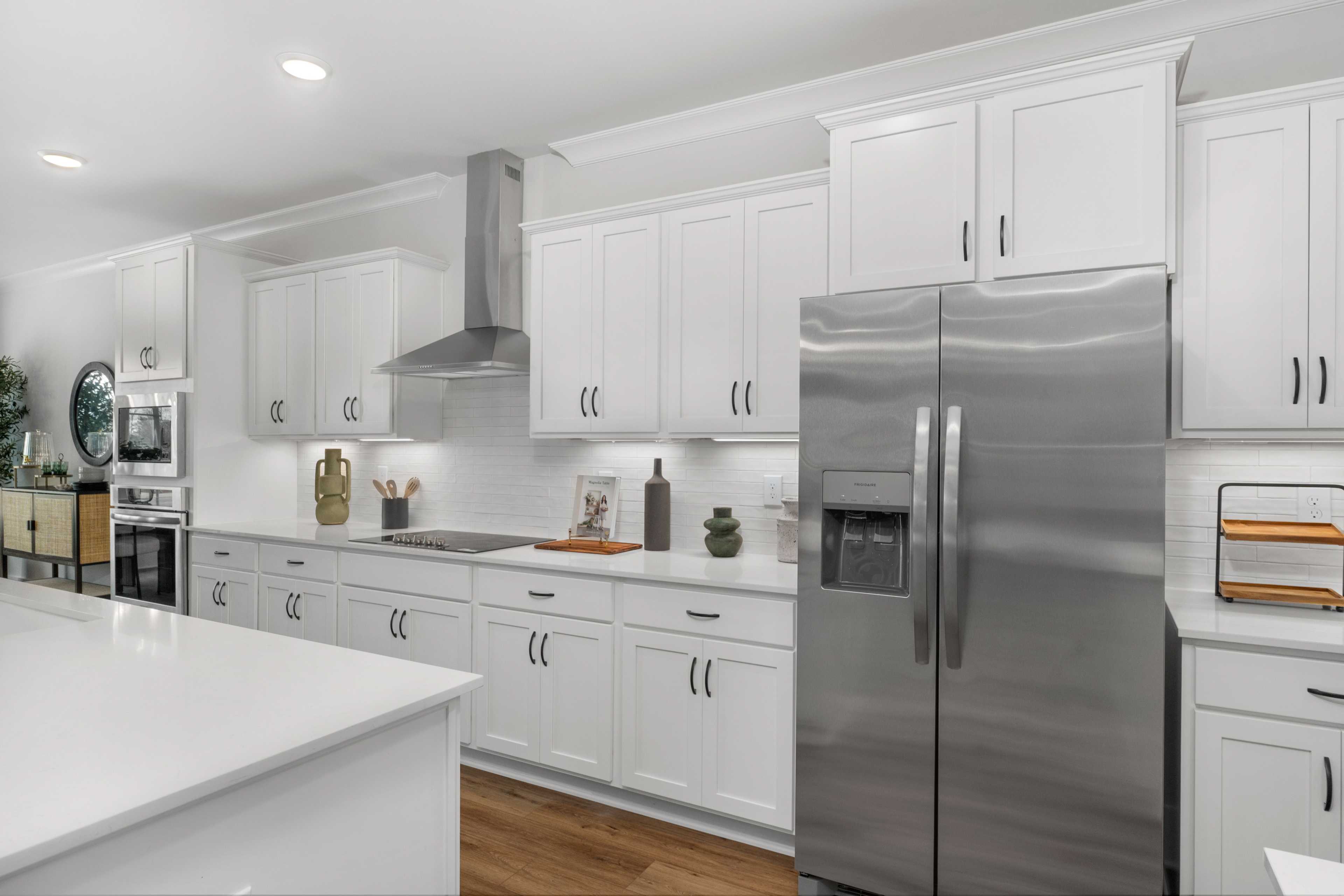Modern white kitchen in Briercreek home by Davidson Homes, Meridianville AL with island, stainless steel fridge, hardwood floors