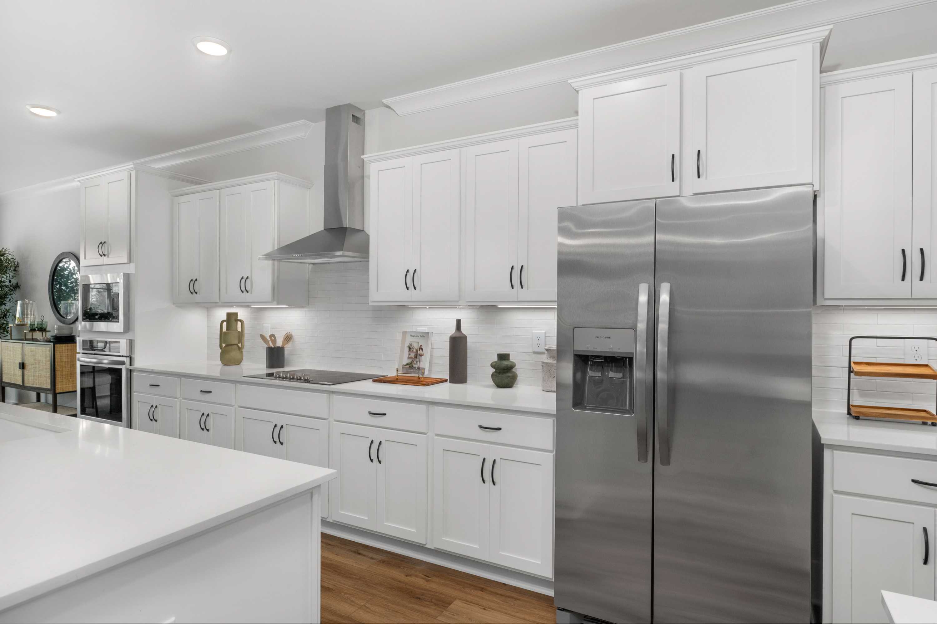 Modern white kitchen in Briercreek home by Davidson Homes, Meridianville AL with island, stainless steel fridge, hardwood floors