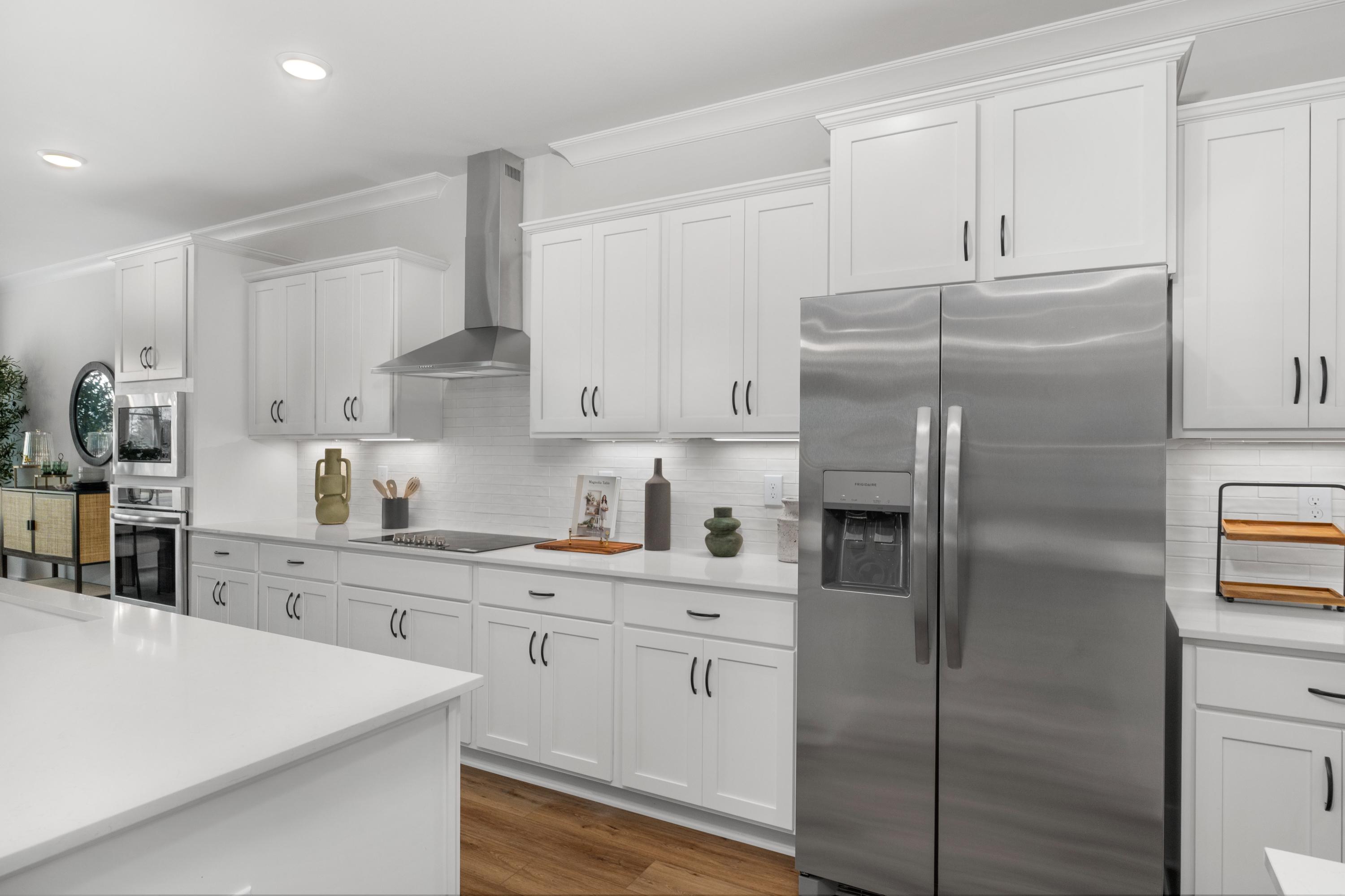 Modern white kitchen in Briercreek home by Davidson Homes, Meridianville AL with island, stainless steel fridge, hardwood floors