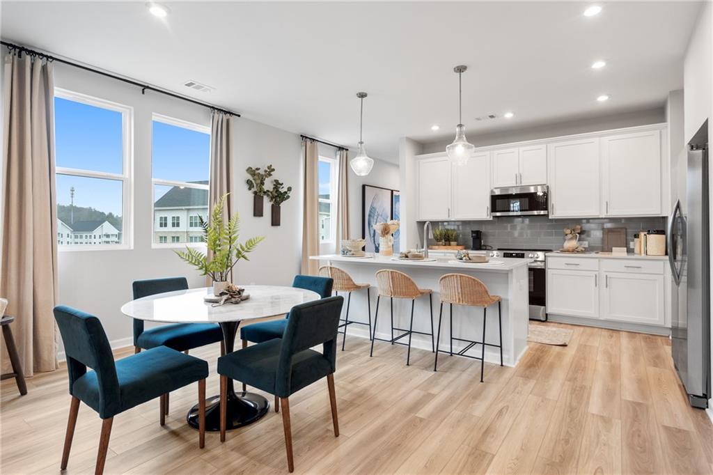 Sunlit dining area with round white table, teal chairs, open to modern white kitchen and island in Wilmington B home, Emerson, GA