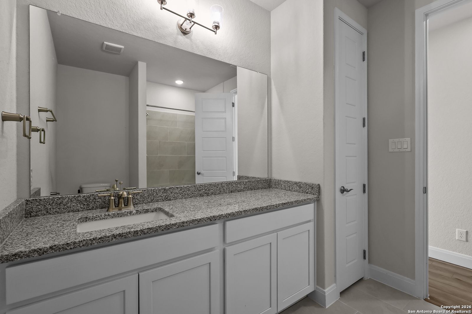 Modern master bathroom with granite countertop vanity, single sink, and large mirror in Davidson Homes The Lanier H, Ladera, San Antonio