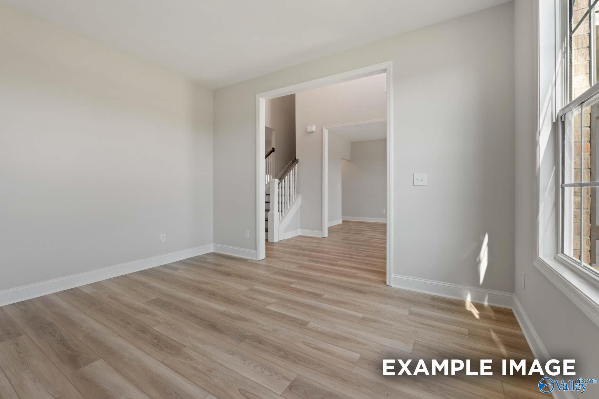 Bright entry foyer with light wood laminate floors, white staircase, and large sunny window in The Madison A home, Toney, Alabama