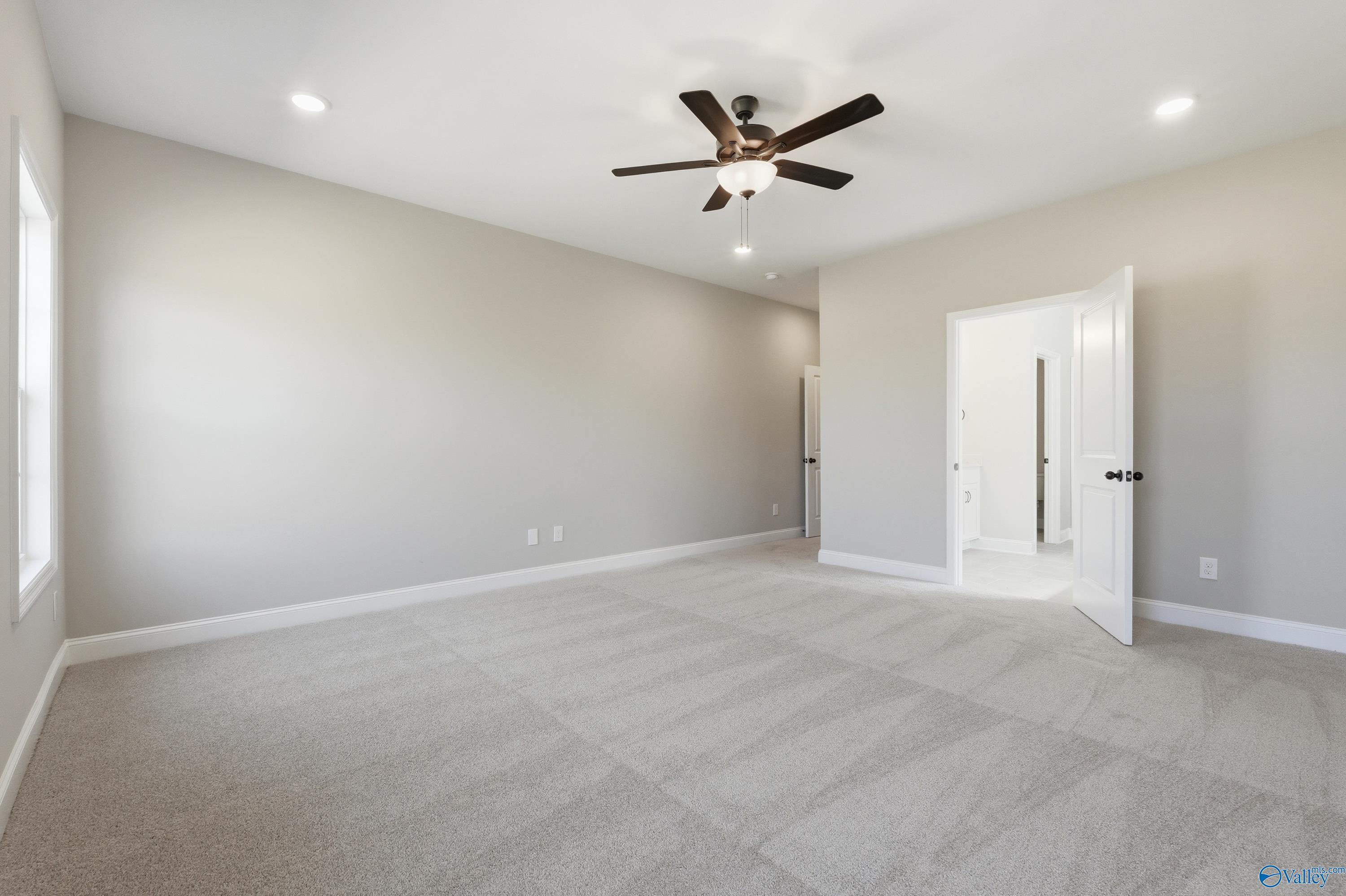 Spacious master bedroom with ceiling fan, beige carpet, and en-suite bath door in Davidson Homes The Rockford, Harvest, Alabama