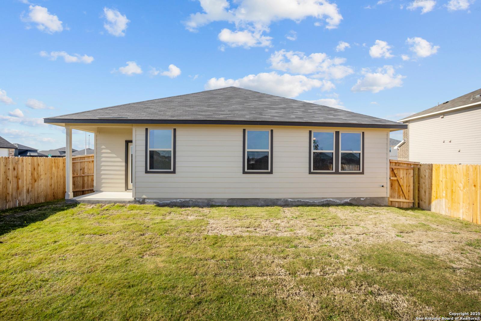 Back view of The Daphne H single-story home with covered patio, large windows, and fenced grassy yard in Hannah Heights, Seguin, Texas