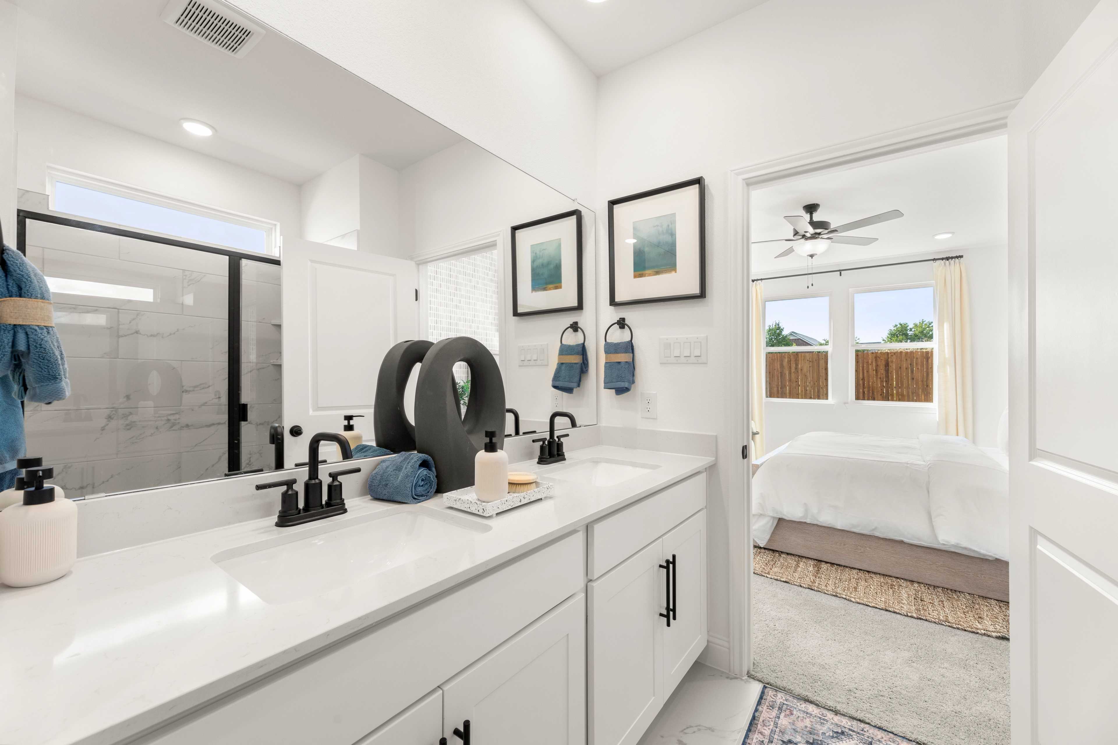 Spacious master bathroom in The Laurel featuring white double vanity, black faucets, walk-in shower, and bedroom view