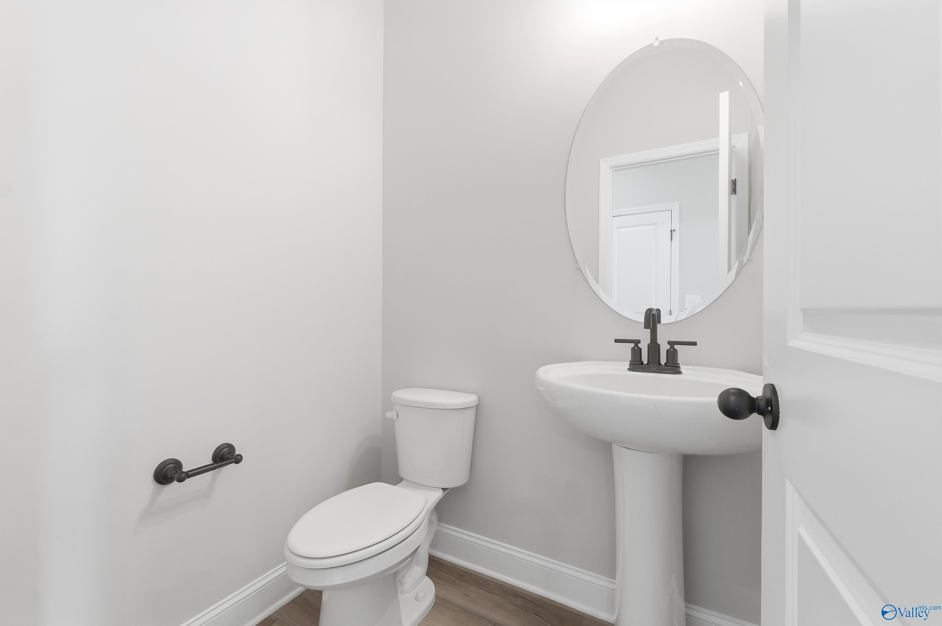 Elegant powder room featuring white pedestal sink, oval mirror, black fixtures, and toilet in Davidson Homes The Rockford C, Athens, Alabama