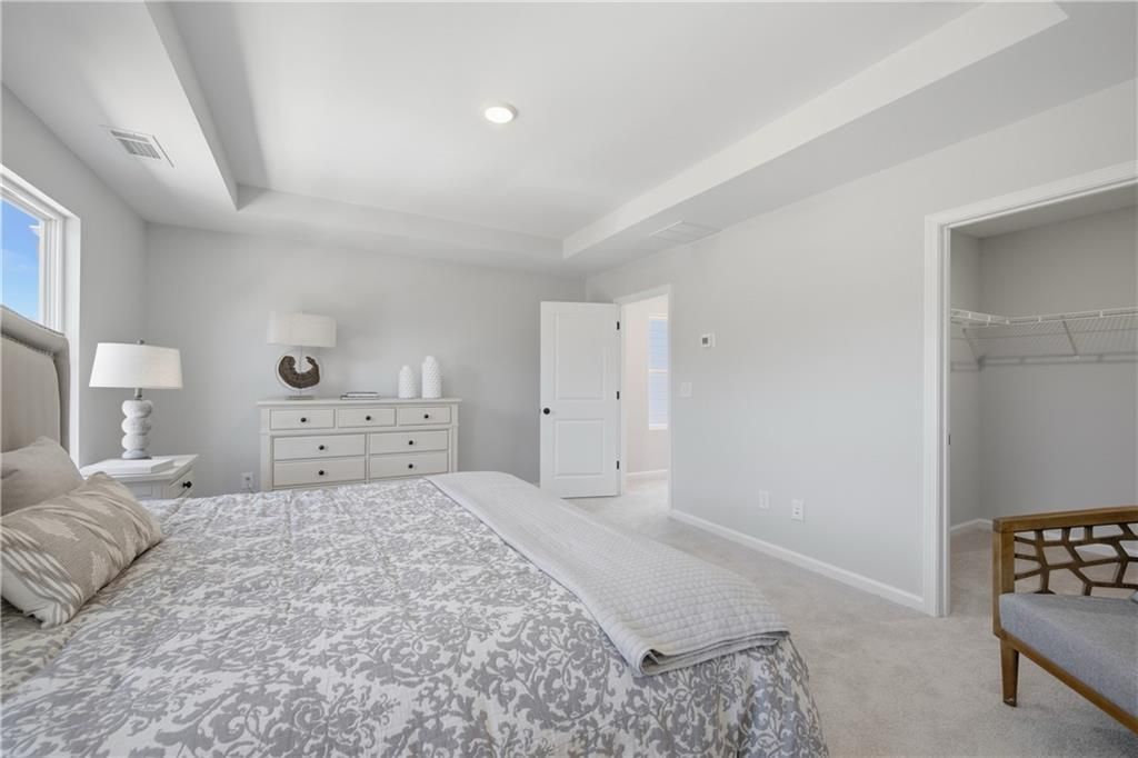 Bright primary bedroom with tray ceiling, upholstered headboard, and walk-in closet in Davidson Homes Hartwell C plan, Canton, GA