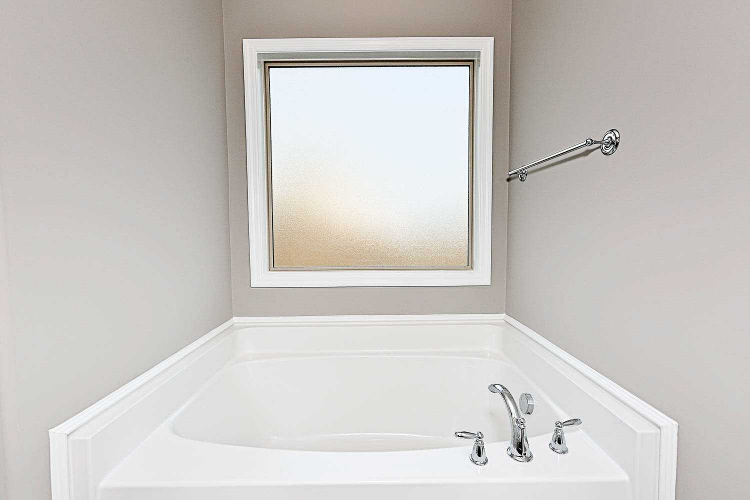 Deep soaking tub in The Montgomery master bathroom with frosted window and chrome faucet, Davidson Homes design