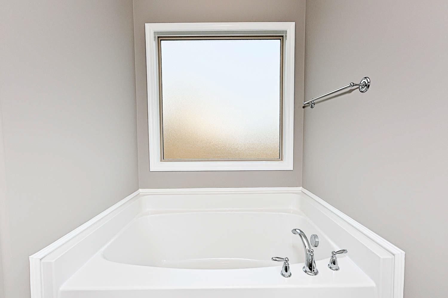 Deep soaking tub in The Montgomery master bathroom with frosted window and chrome faucet, Davidson Homes design