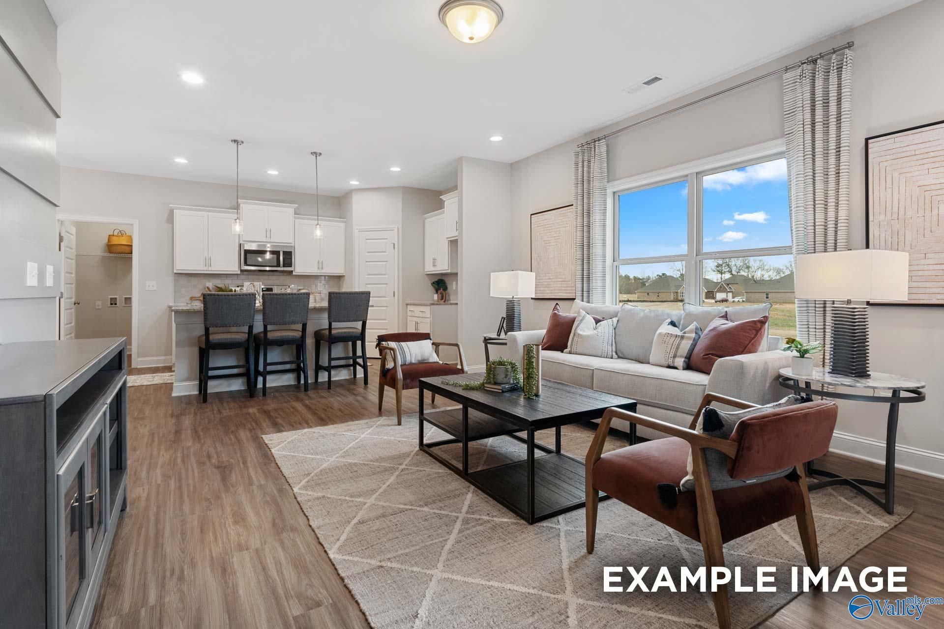 Open-concept living room and kitchen with white cabinets and bar seating in Davidson Homes Camilla C, Hartselle, Alabama