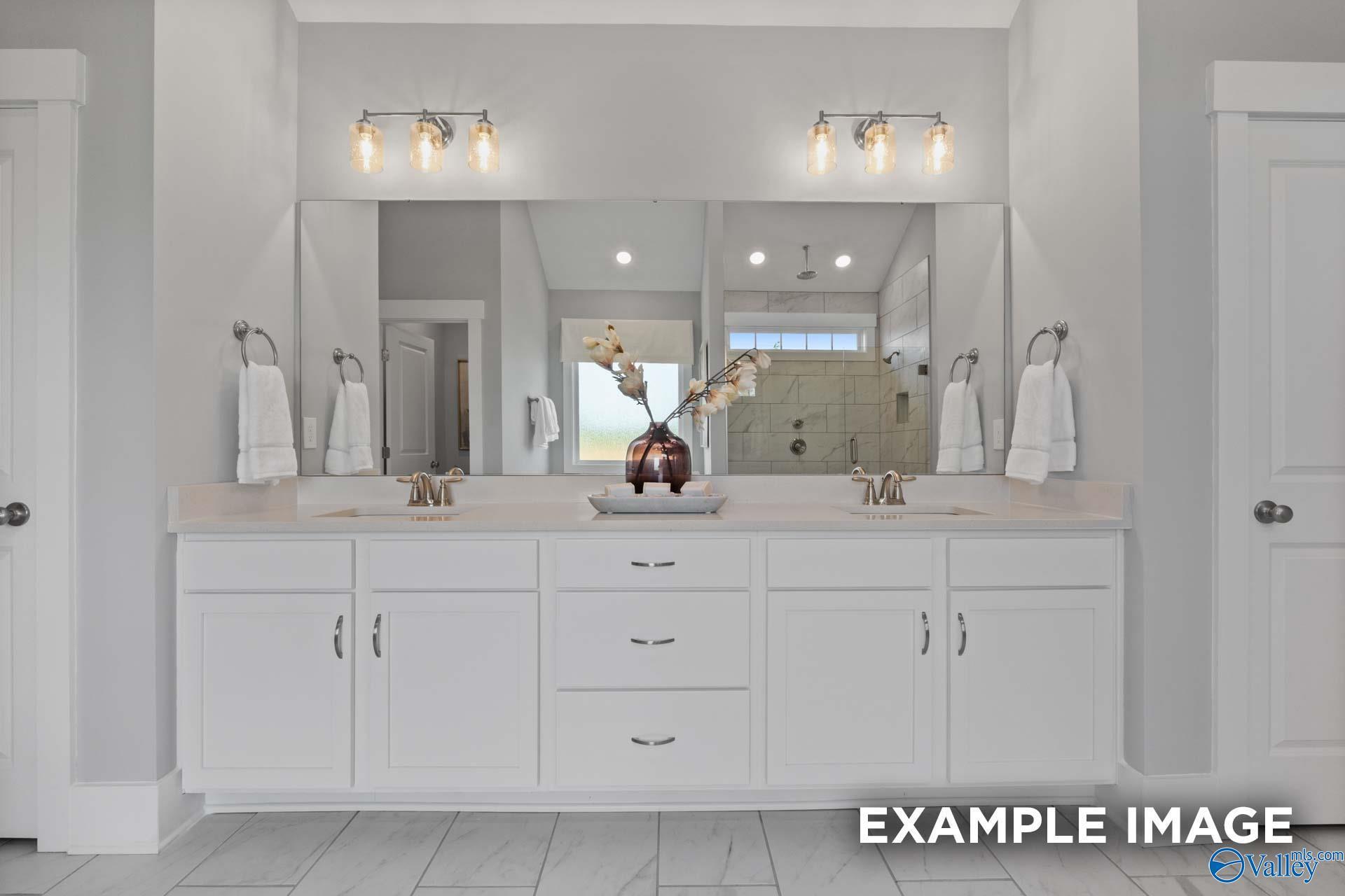 Elegant master bathroom double vanity with white cabinets, dual sinks, mirrors, and floral accents in Davidson Homes The Finleigh, Huntsville AL