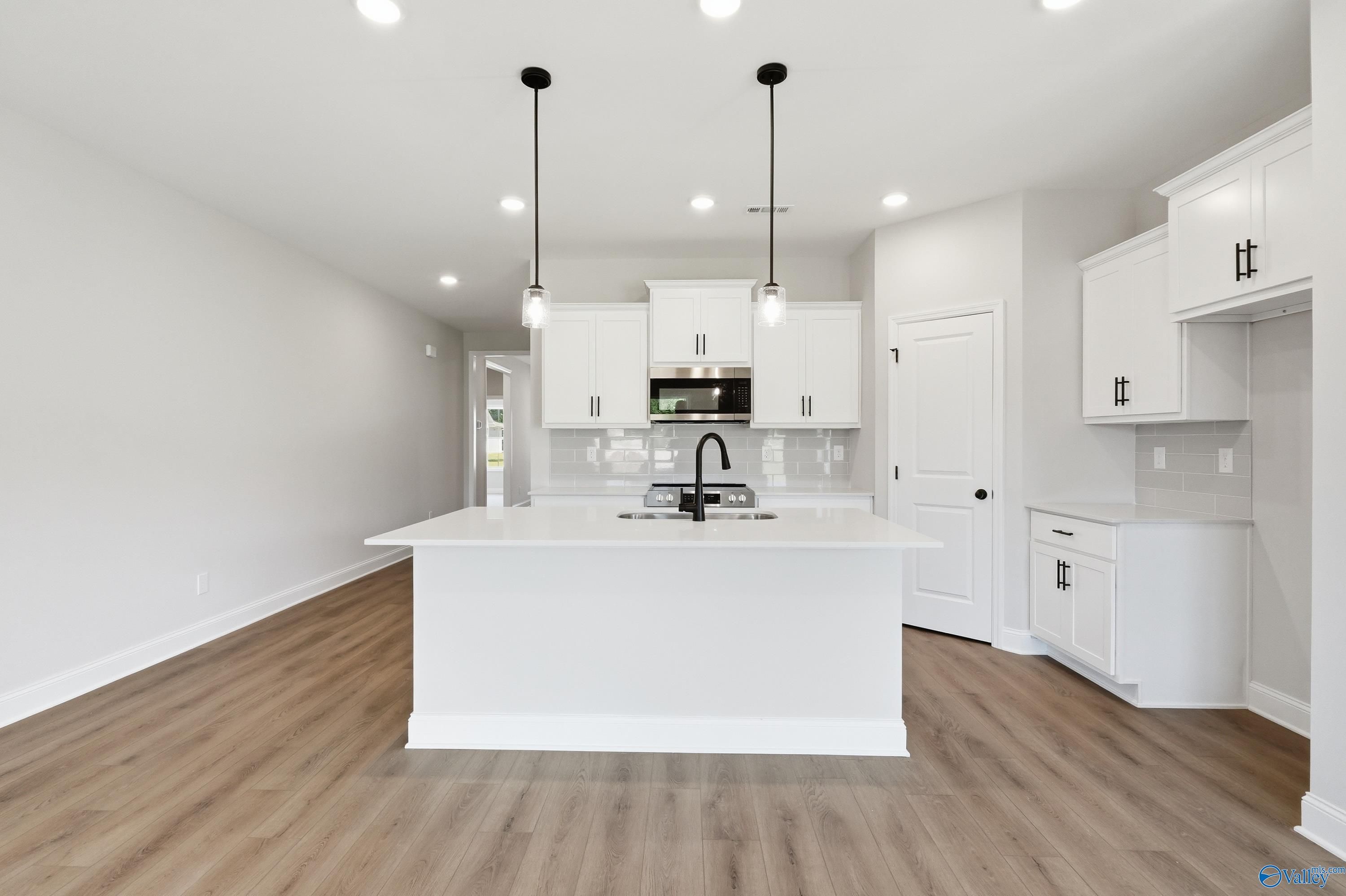 Modern kitchen with white cabinets, quartz island, and pendant lighting in The Daphne F floor plan, Forest Glen, Alabama.