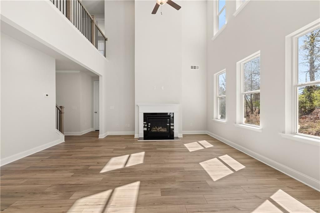 Two-story great room featuring vaulted ceiling, gas fireplace, hardwood floors, and large windows in Davidson Homes Danbury C, Buford, GA