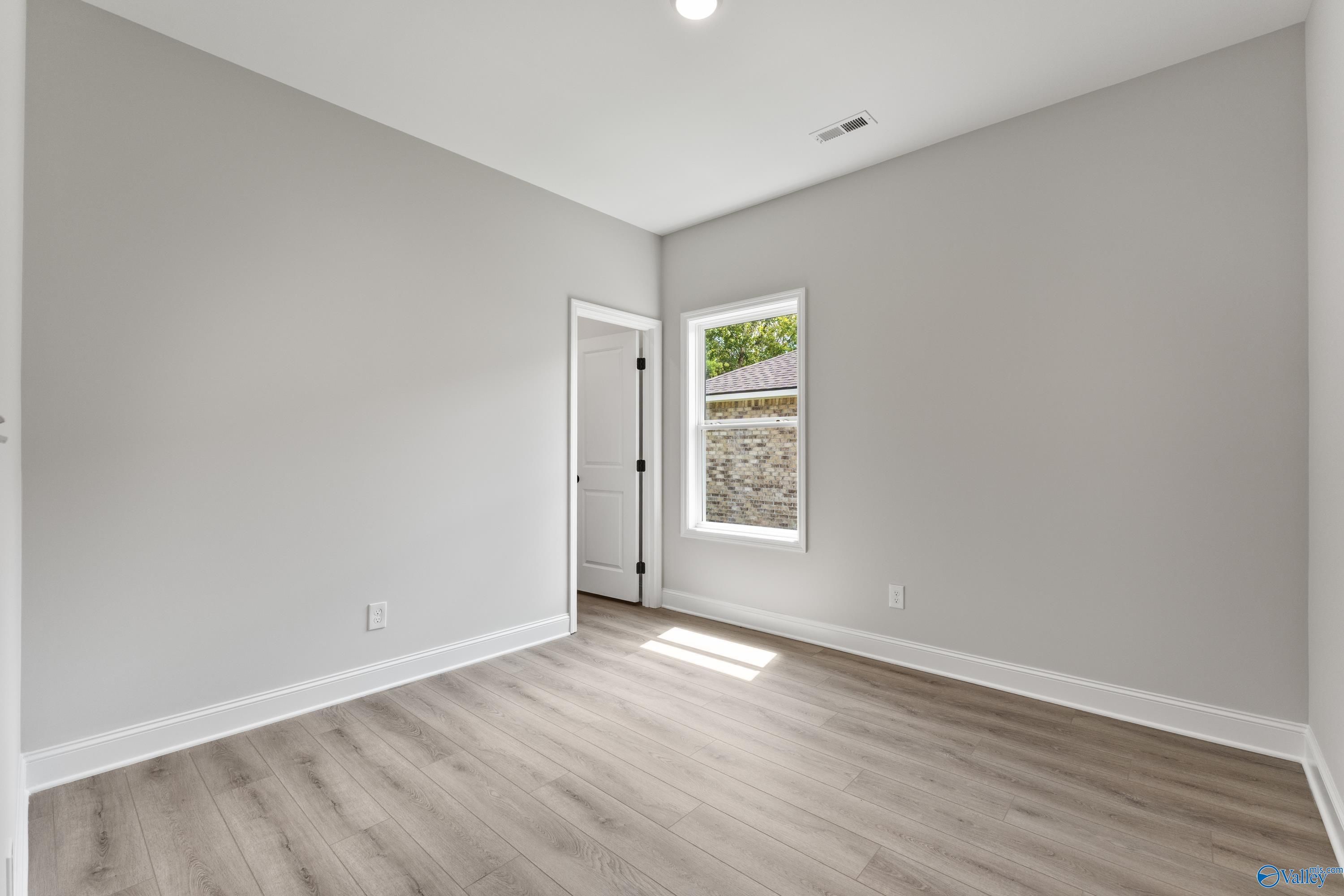 Bright empty secondary bedroom with gray walls, large window, and luxury vinyl plank flooring in Davidson Homes The Daphne, Huntsville, AL