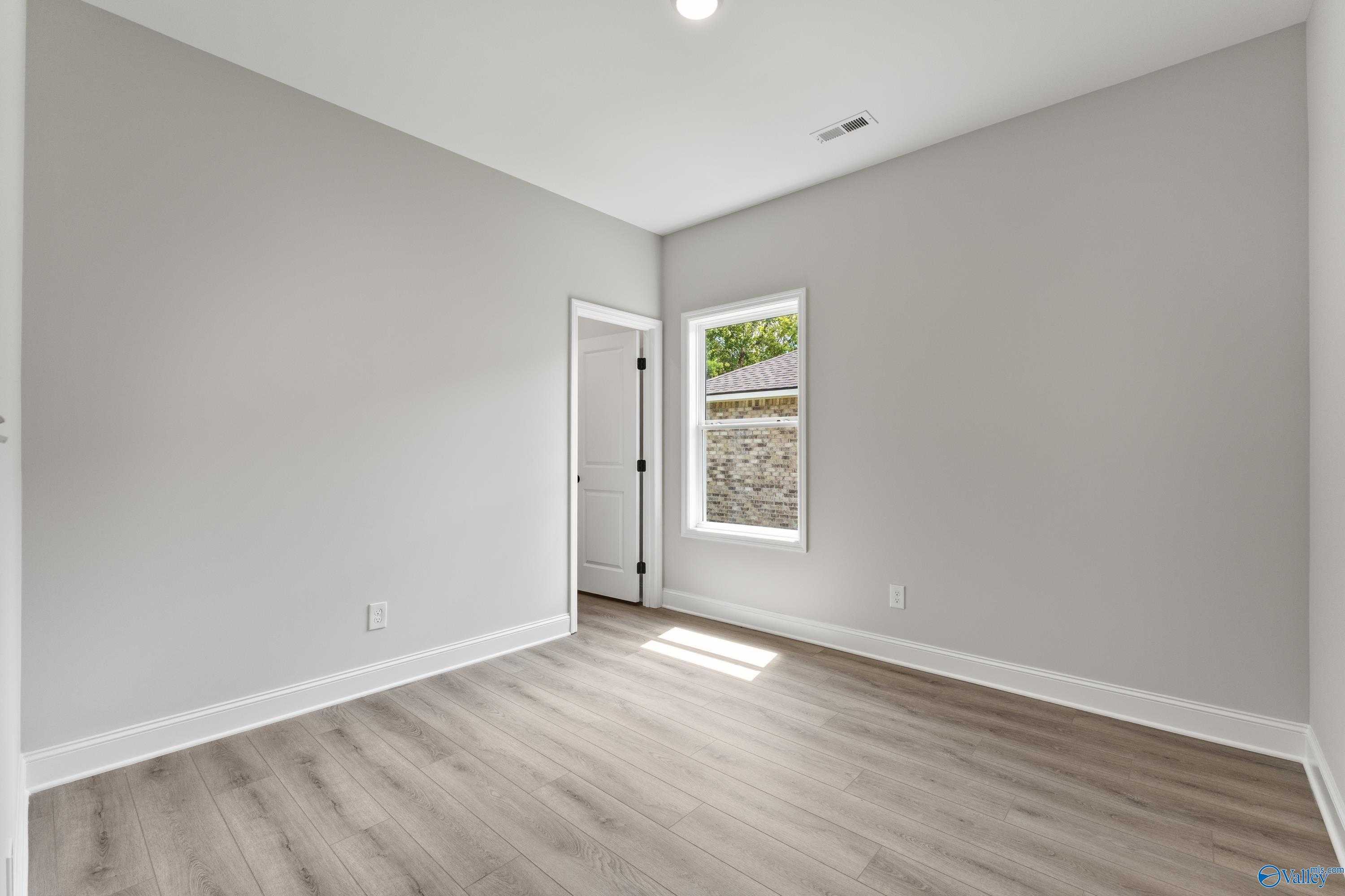 Bright empty secondary bedroom with gray walls, large window, and luxury vinyl plank flooring in Davidson Homes The Daphne, Huntsville, AL