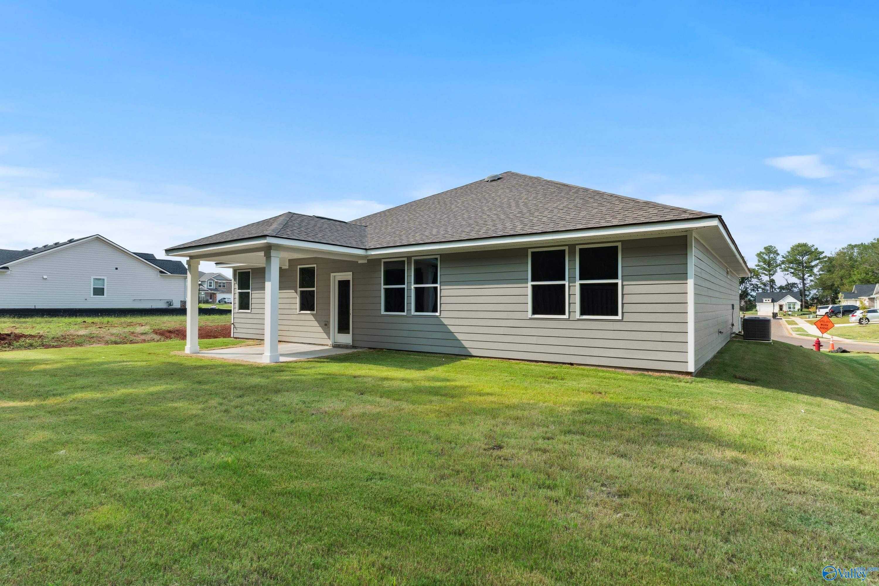 Side view of single-story beige home with covered patio, double windows, and green lawn in Evergreen Mill, Madison, Alabama - Evermore Homes The Grace