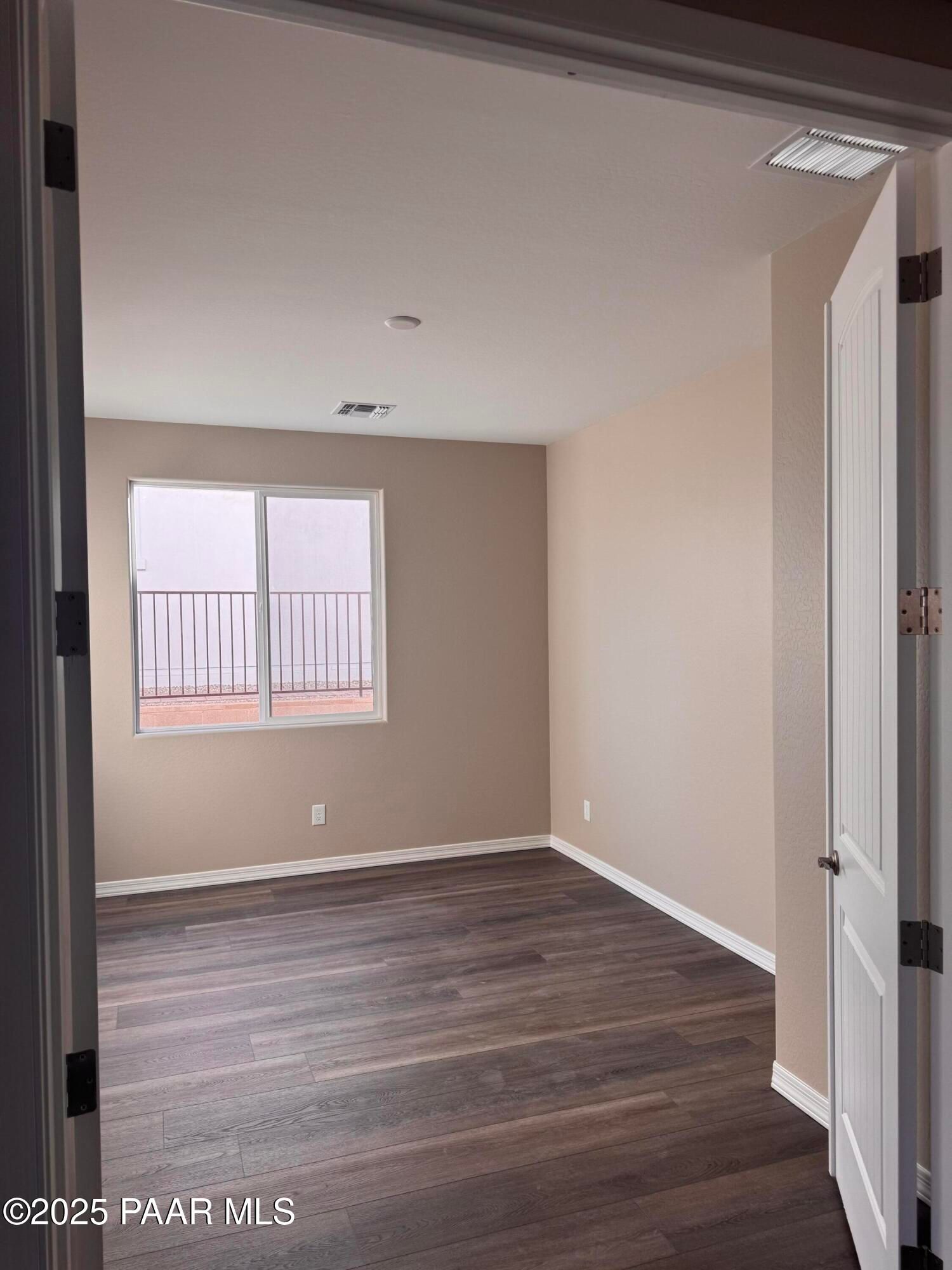 Spacious empty bedroom with beige walls, dark laminate flooring, and balcony window in Davidson Homes The Sunrise II A, Prescott, Arizona