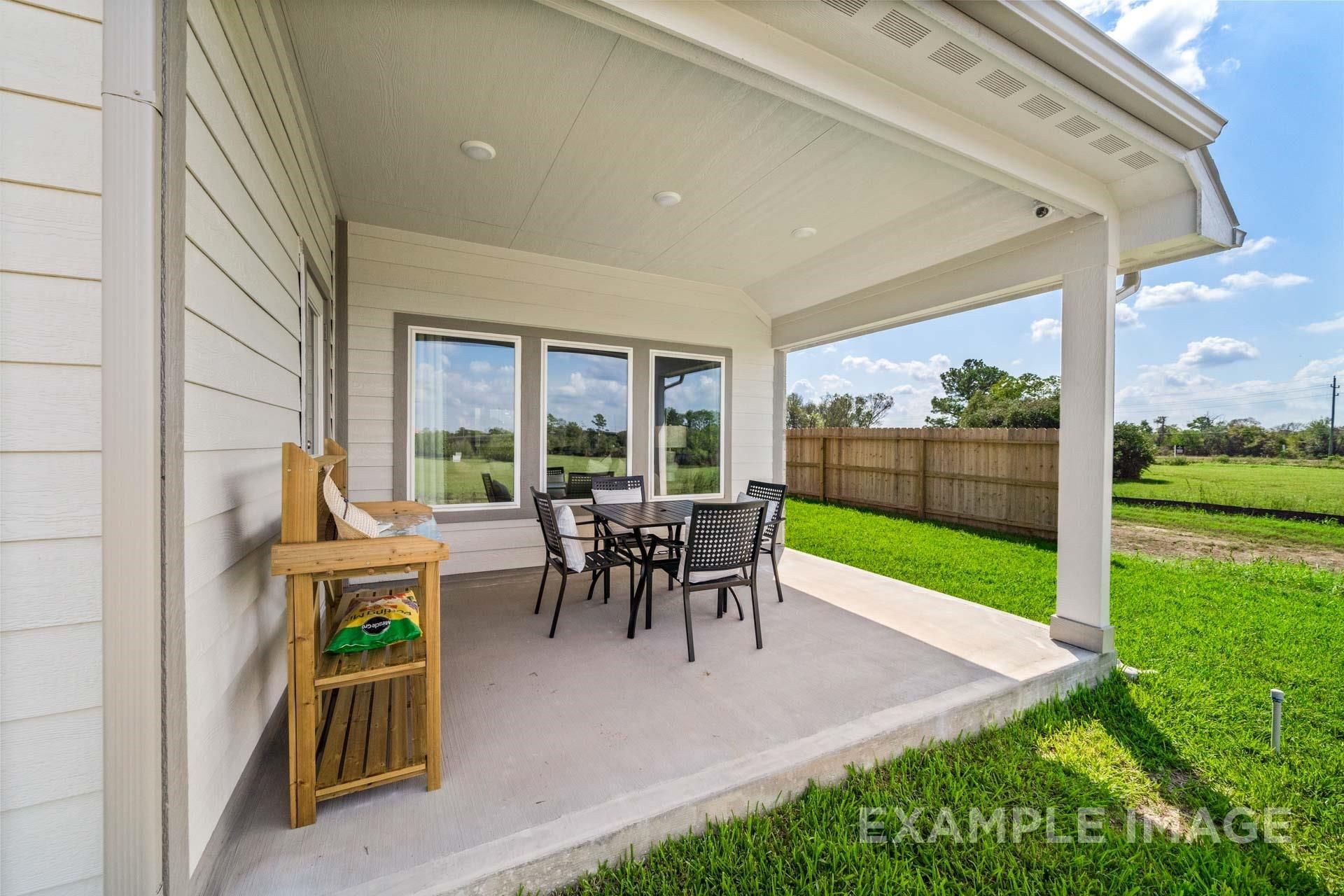 Covered back patio with wicker seating and snack table overlooking lush green backyard in Davidson Homes The Acadia A, Lago Mar, Texas City