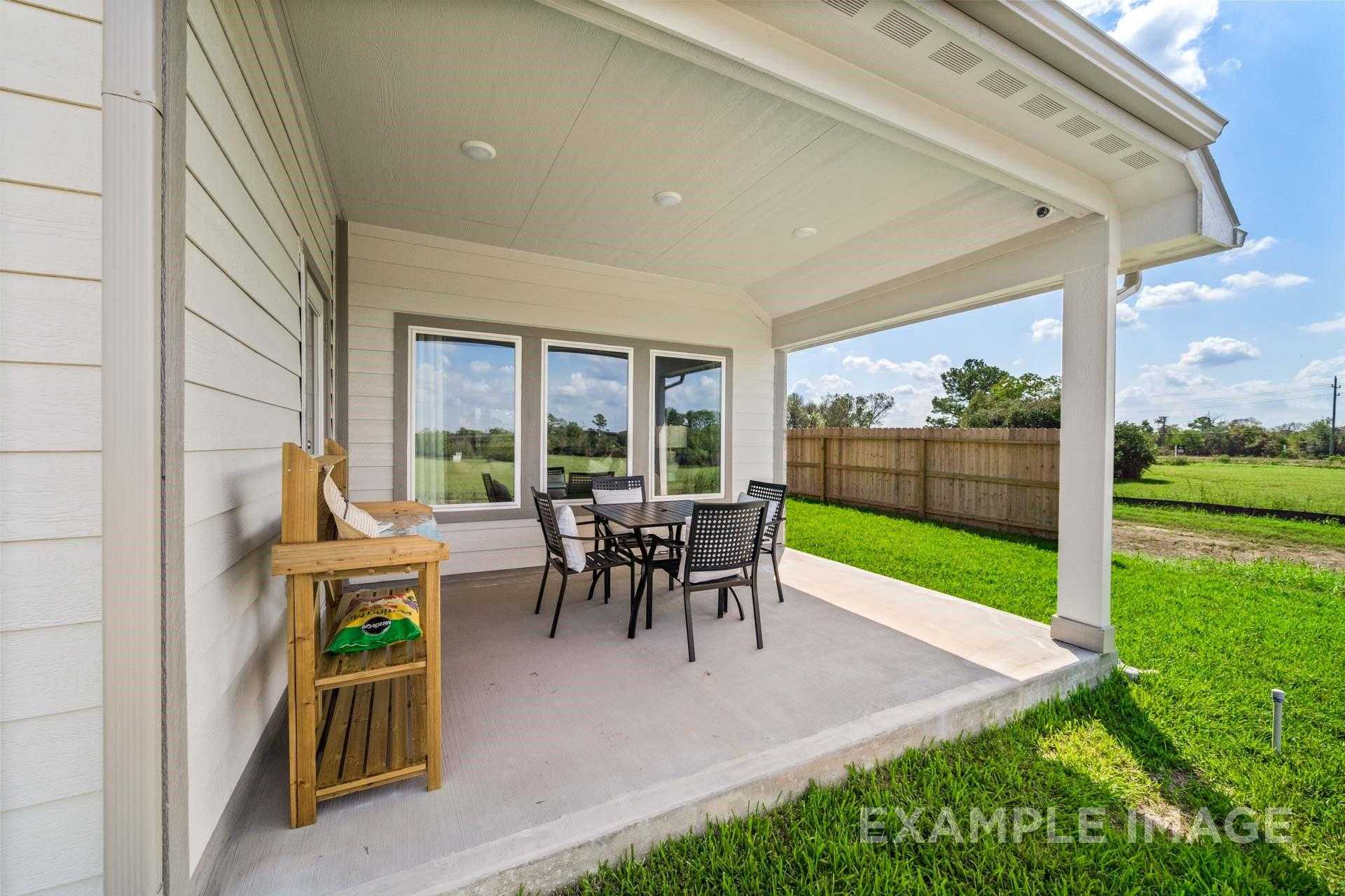 Covered back patio with wicker dining set and wooden sideboard overlooking green lawn in Davidson Homes The Acadia A, Lago Mar, Texas City
