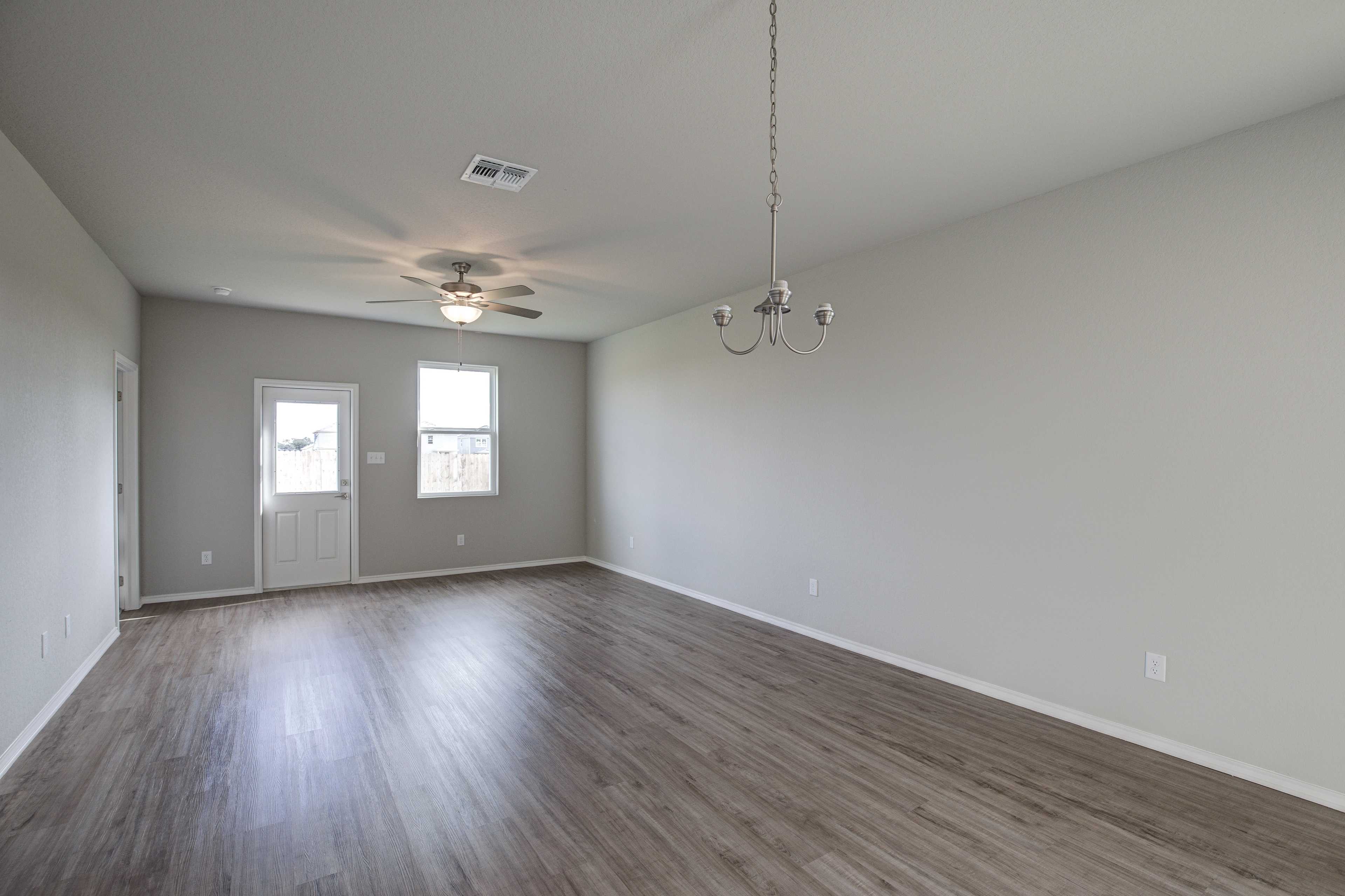 Spacious open-concept living room in The Frio B by Davidson Homes featuring light gray walls, hardwood floors, ceiling fan, and chandelier