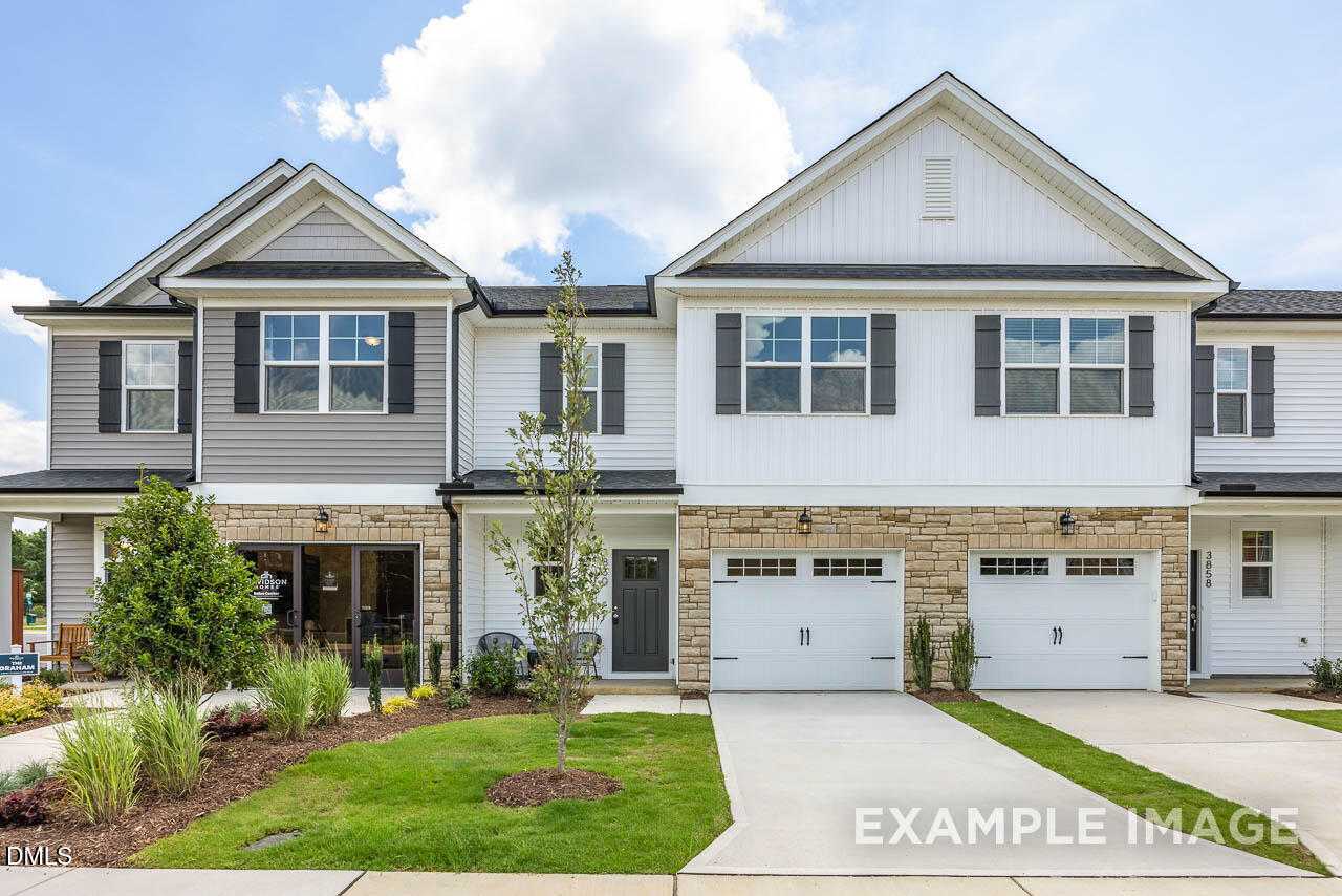 Modern two-story townhome exterior with gray siding, 1-car garage, stone accents, and landscaped yard in Springvale, Fuquay-Varina, NC