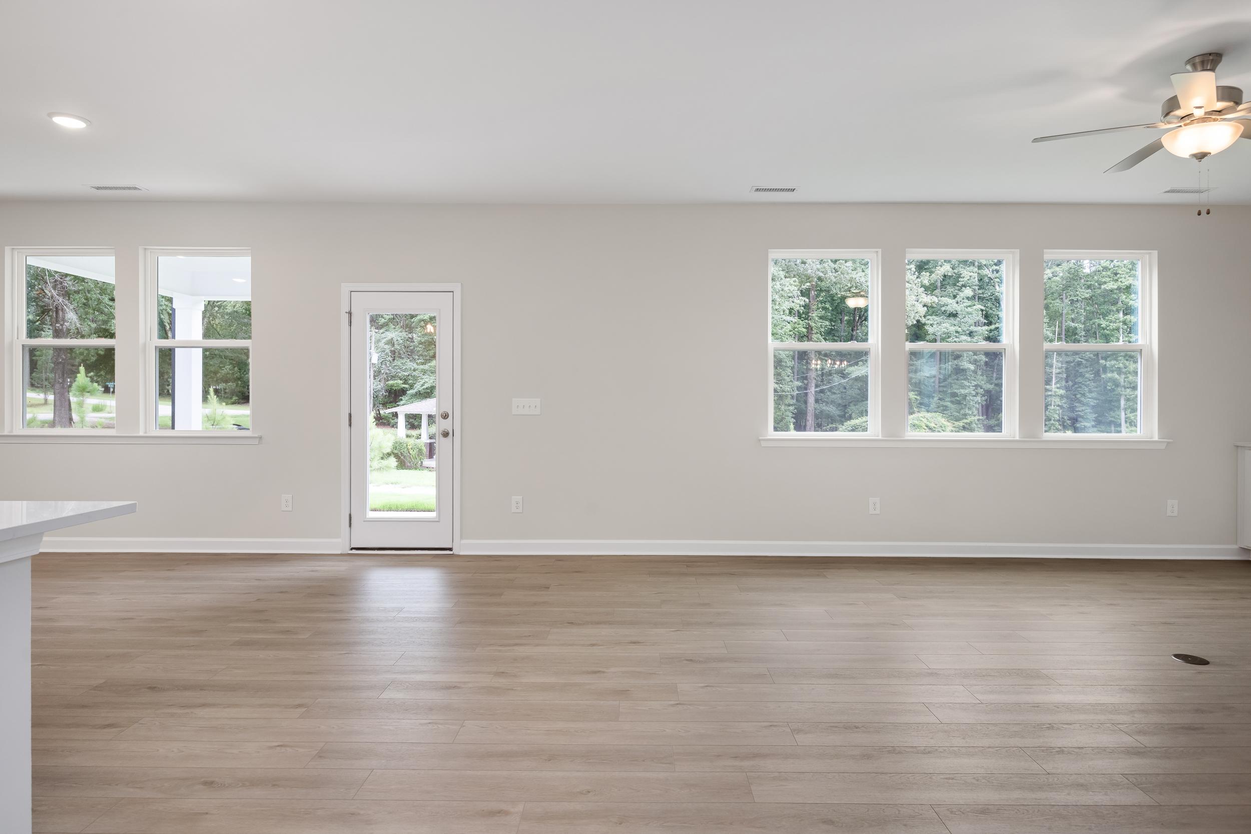 Spacious open-concept great room in The Beech A with hardwood floors, large windows, ceiling fans, and white island