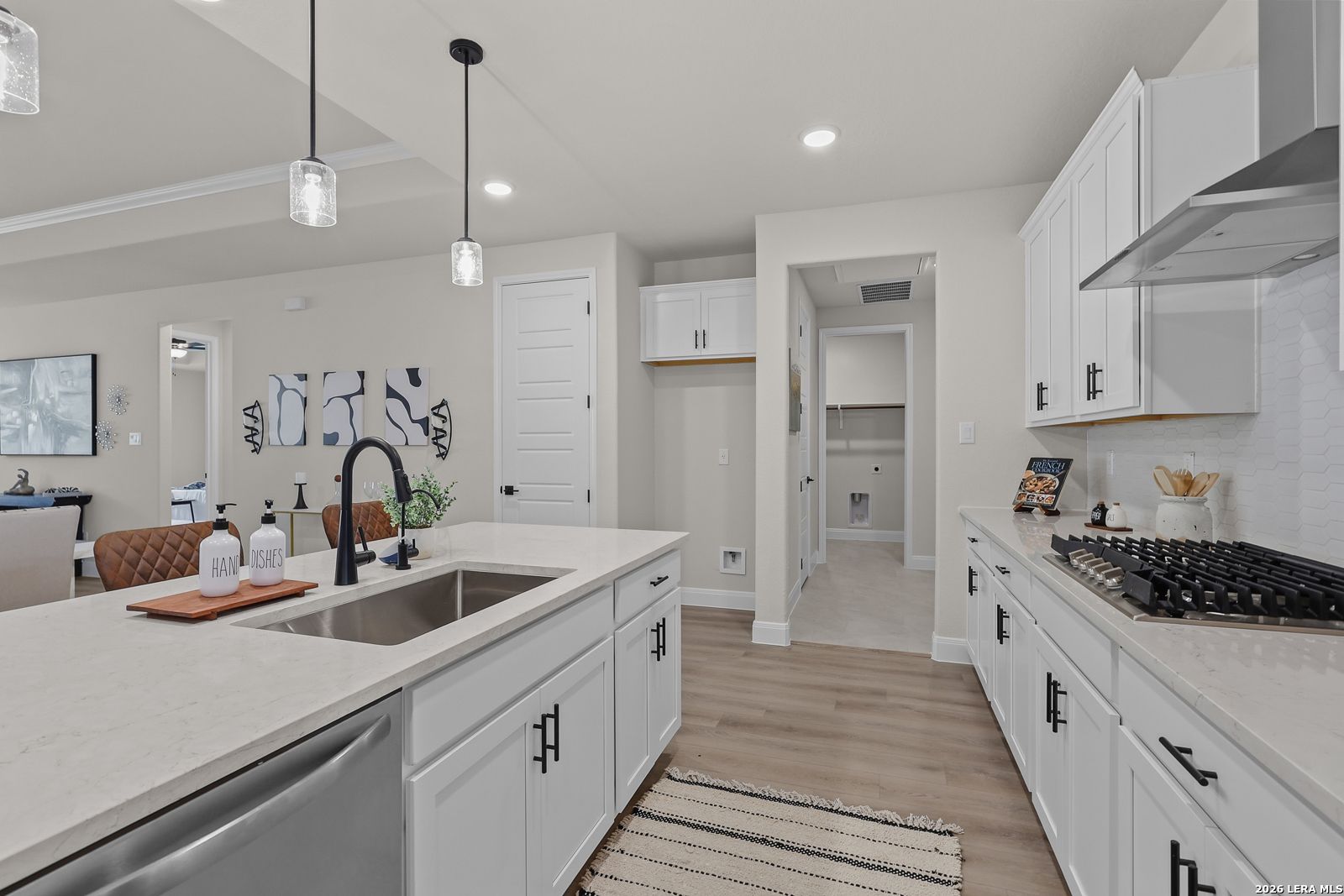 Bright open-concept kitchen with white shaker cabinets, quartz countertops, stainless gas range and island sink in The Lanier G home, Castroville TX