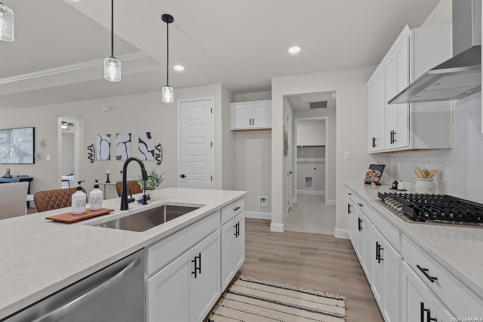 Bright open-concept kitchen with white shaker cabinets, quartz countertops, stainless gas range and island sink in The Lanier G home, Castroville TX