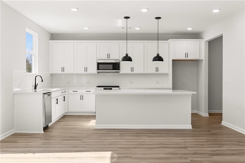 Modern white kitchen with large island, stainless steel appliances, and pendant lights in The Hickory B by Davidson Homes, Winder, GA