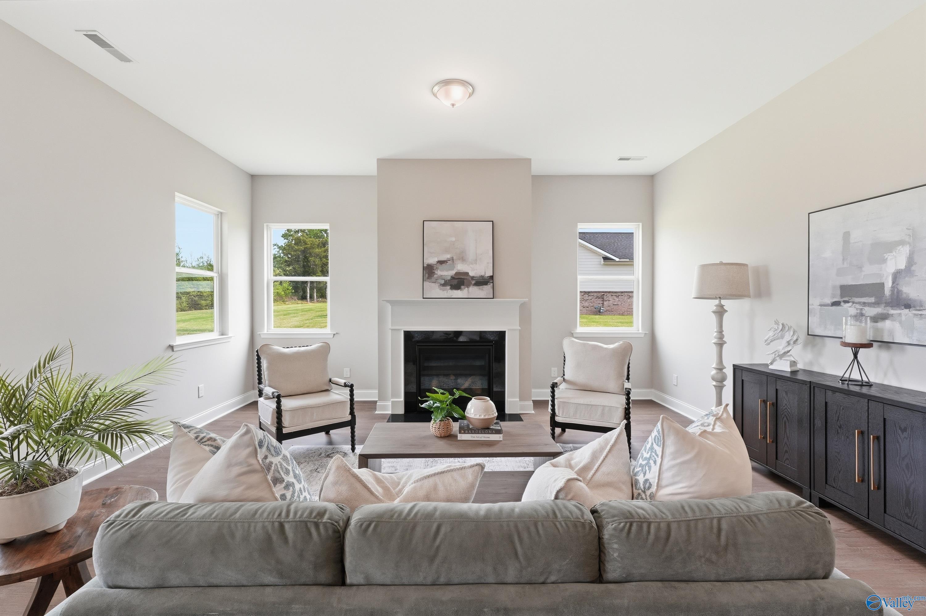 Cozy living room featuring gas fireplace, gray sectional sofa, cream armchairs, and large windows in Davidson Homes The Arcadia B, Huntsville
