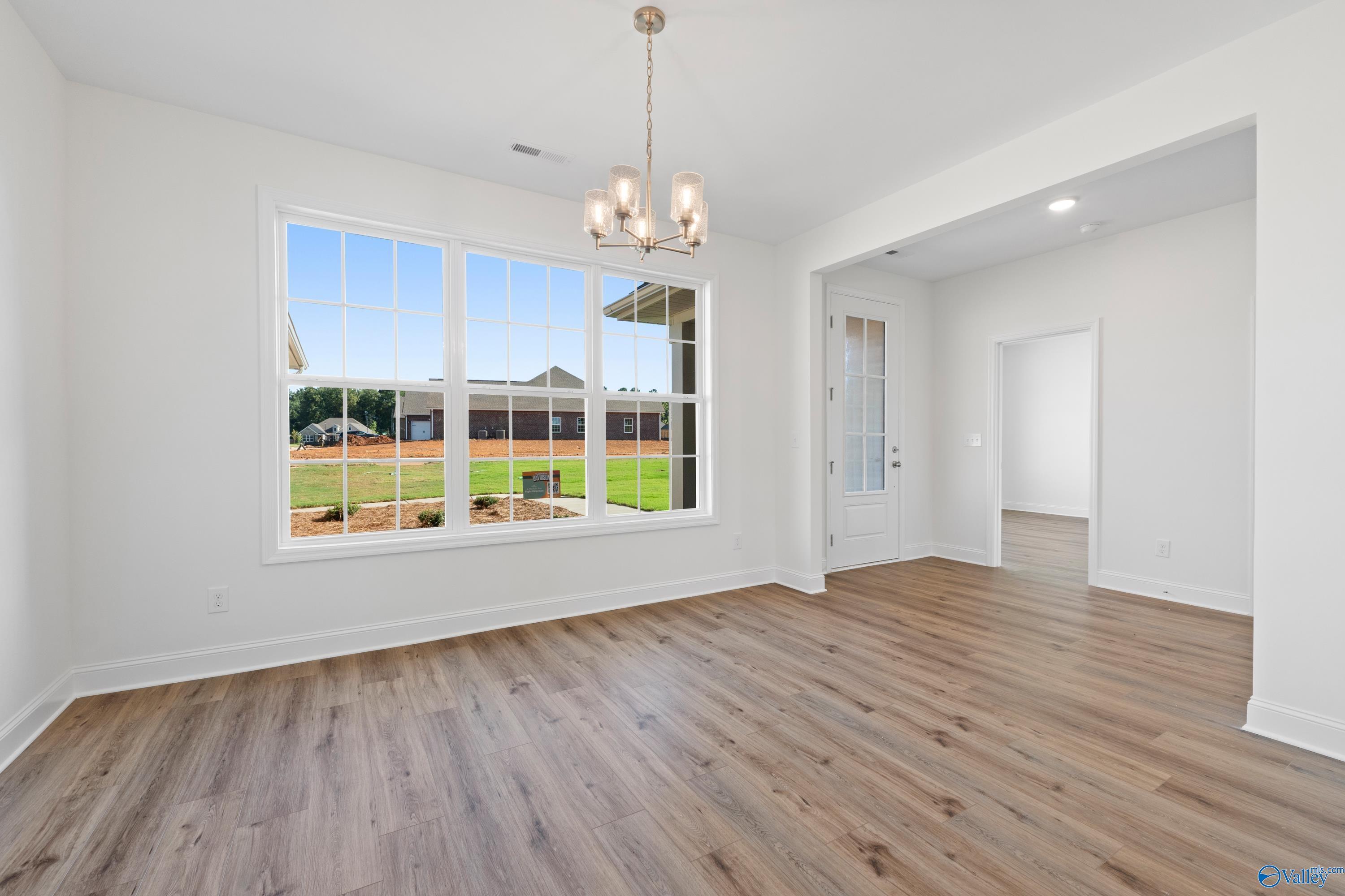 Bright dining room with large windows overlooking lush green lawn, hardwood floors, and elegant chandelier in Davidson Homes The Oxford, Harvest AL
