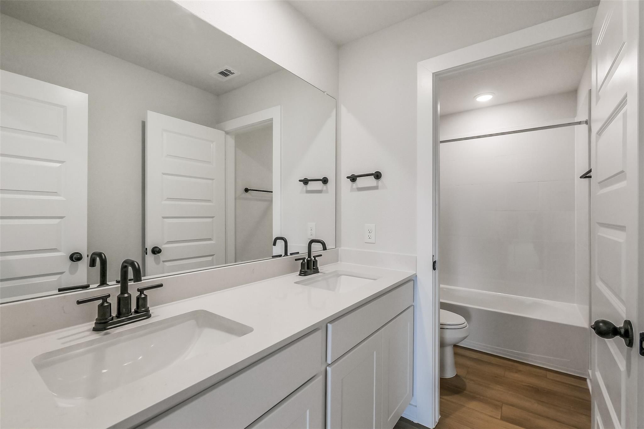 Modern bathroom with white double vanity, soaking tub, walk-in shower, and black fixtures in Davidson Homes Tierra B, Beasley, Texas
