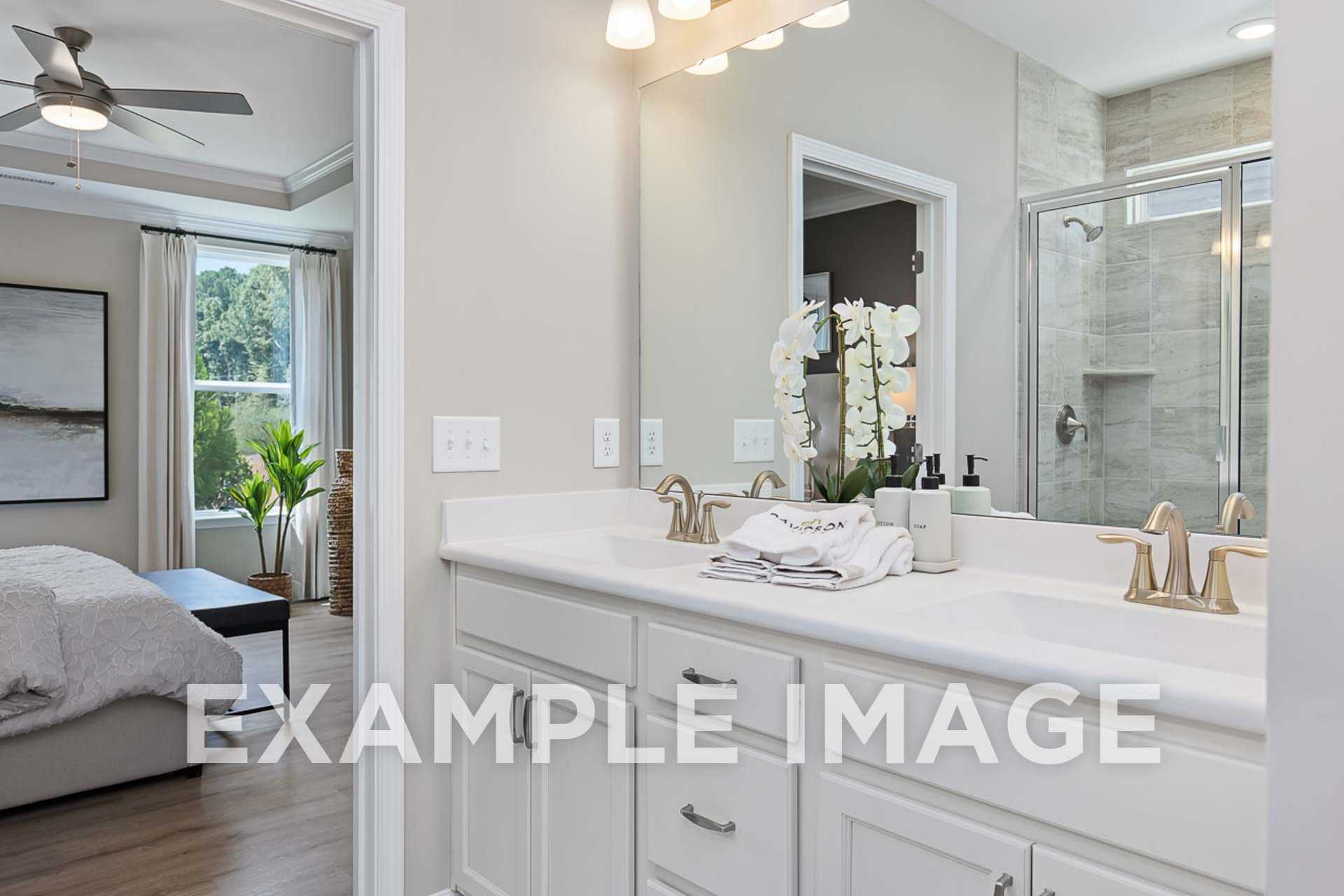 Spacious master bathroom in The Ash E with double vanity, orchids, frameless glass shower, and adjacent bedroom view