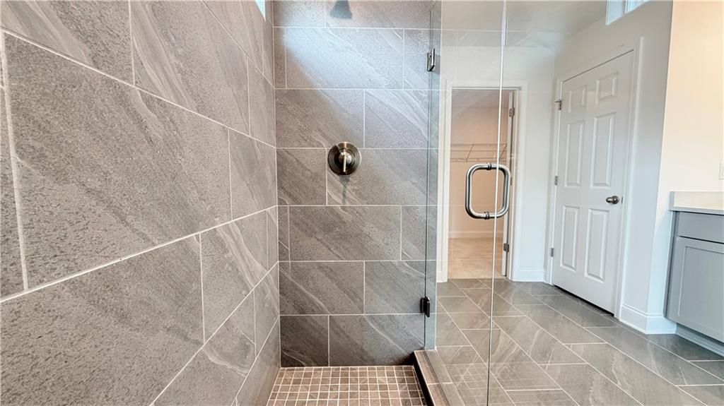 Modern walk-in shower with gray tile and glass door in The Hickory C floor plan at Wehunt Meadows, Hoschton, Georgia.