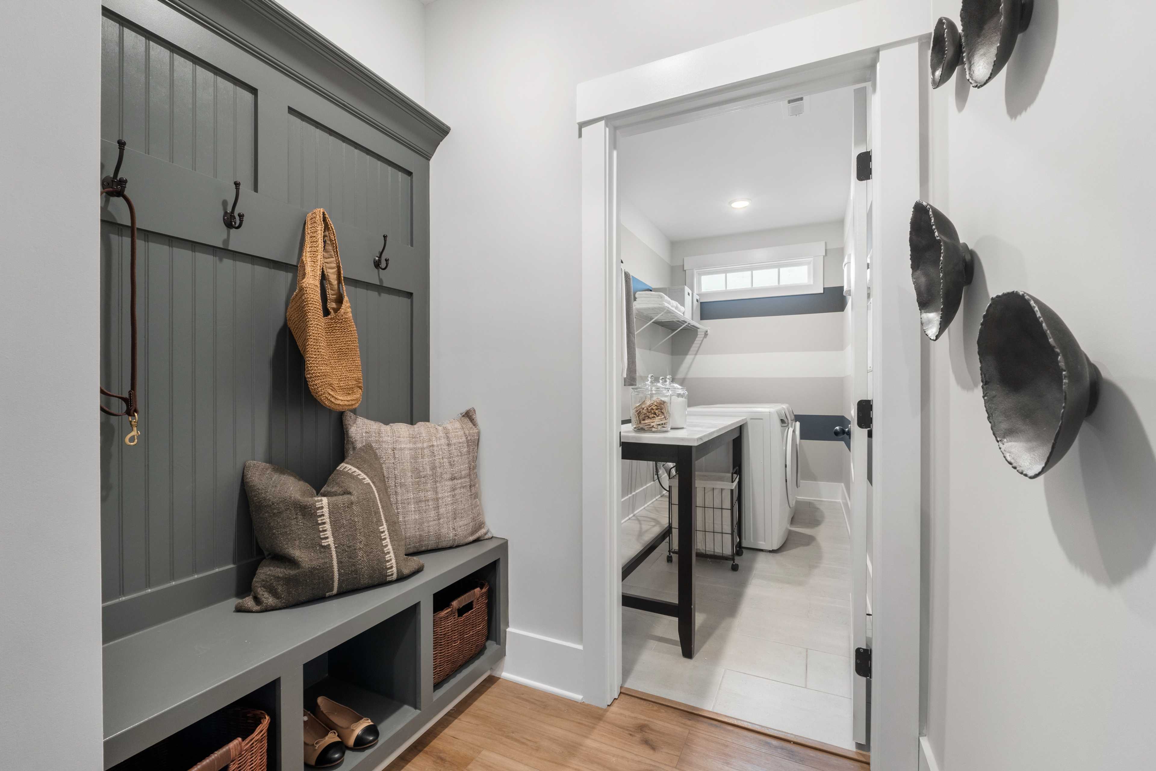 Spacious mudroom at Kendall Farms in Toney AL with gray shiplap cabinetry, built-in bench, hooks, pillows, baskets, and laundry room access