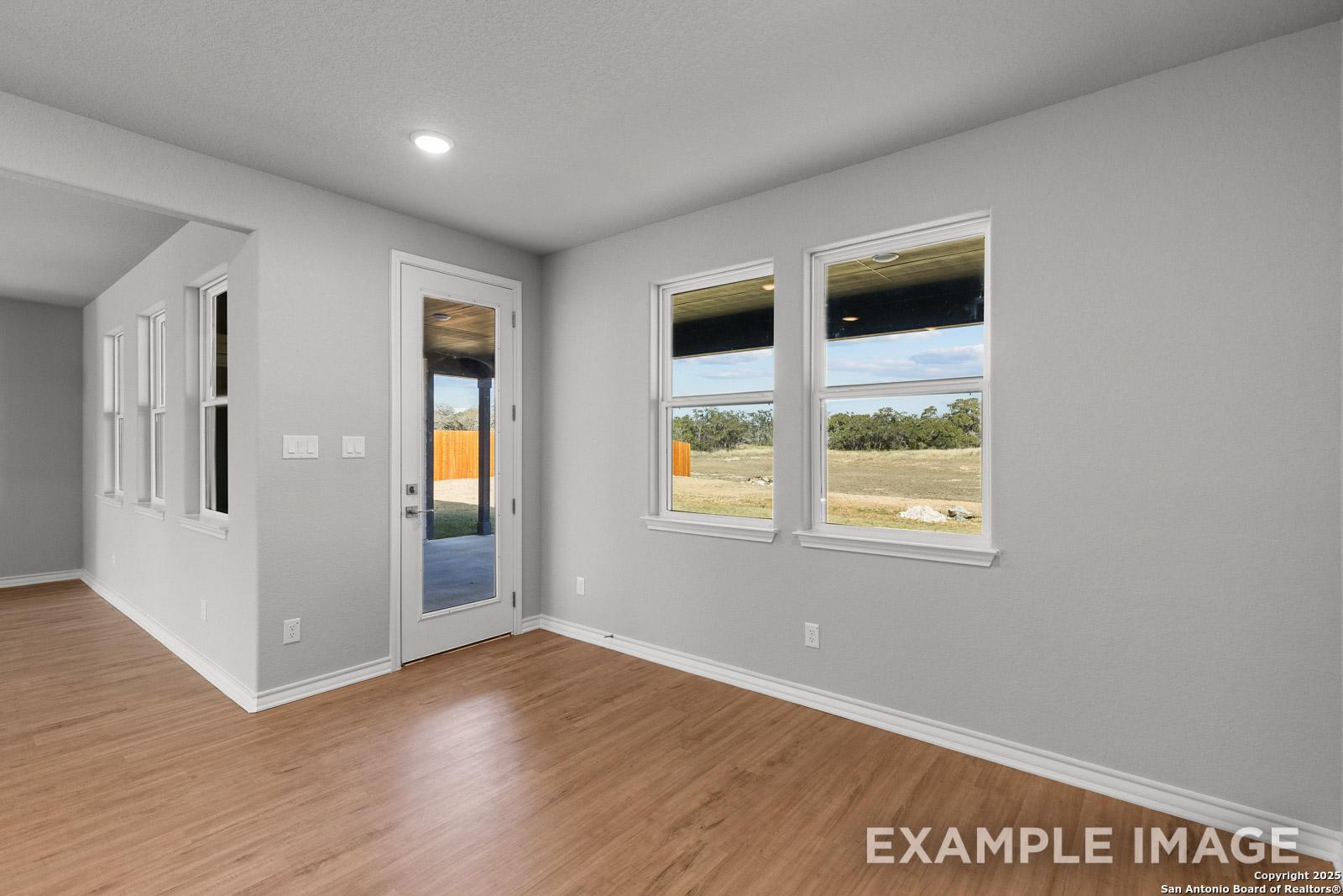 Bright living area in The Oxford H with wood-look flooring, large windows, and glass door access to the covered patio.