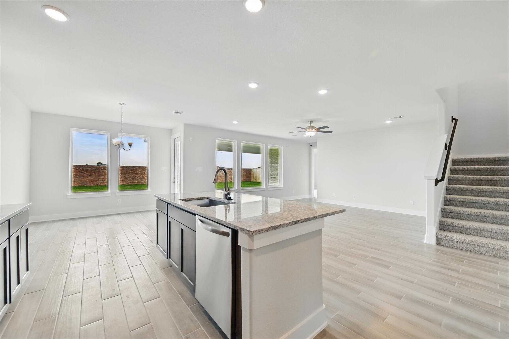 Open-concept kitchen with granite island, stainless dishwasher, and large windows to backyard in Davidson Homes The Philip A, Texas City