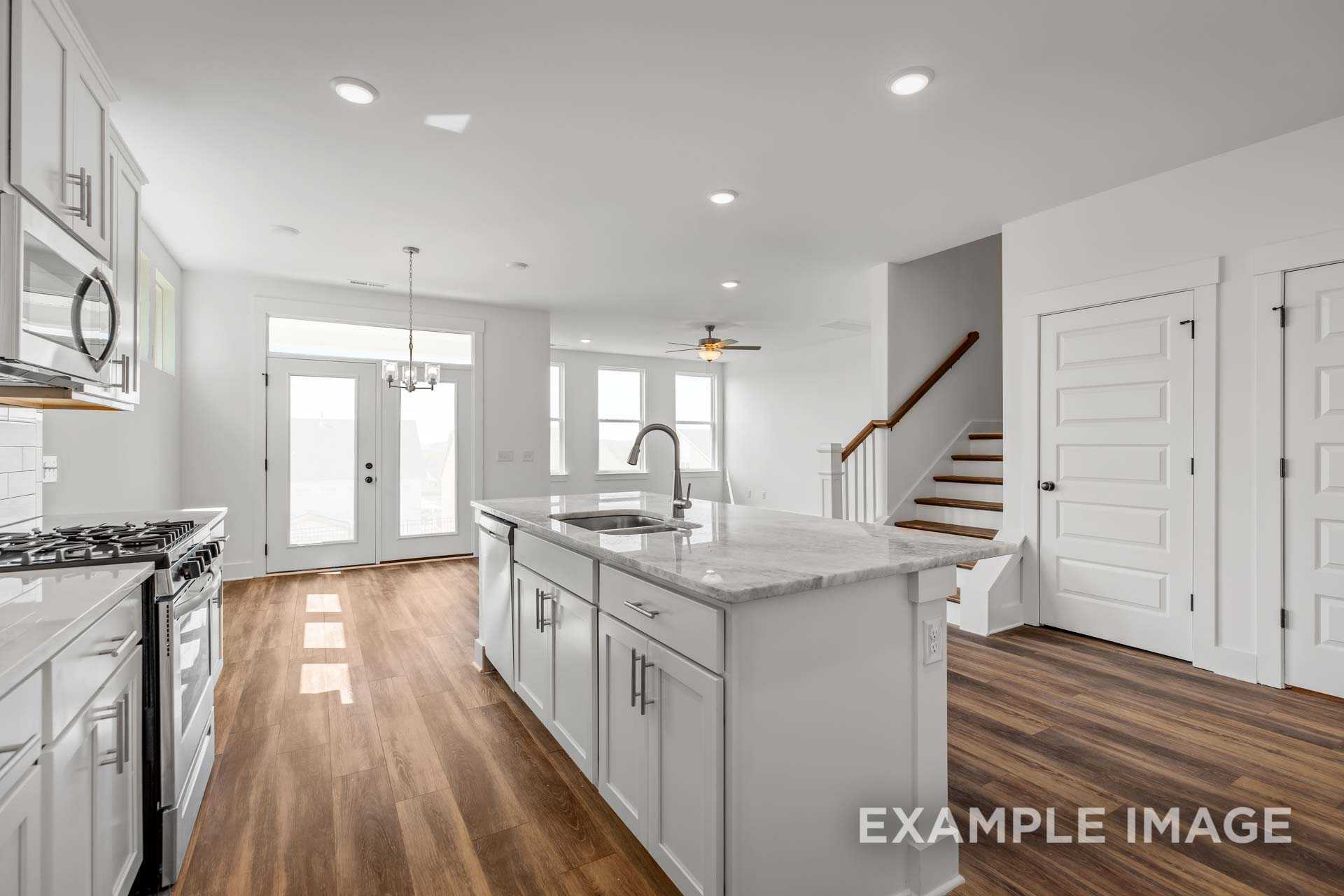 Open-concept kitchen in The Ash C with white shaker cabinets, marble island sink, gas range, and hardwood floors