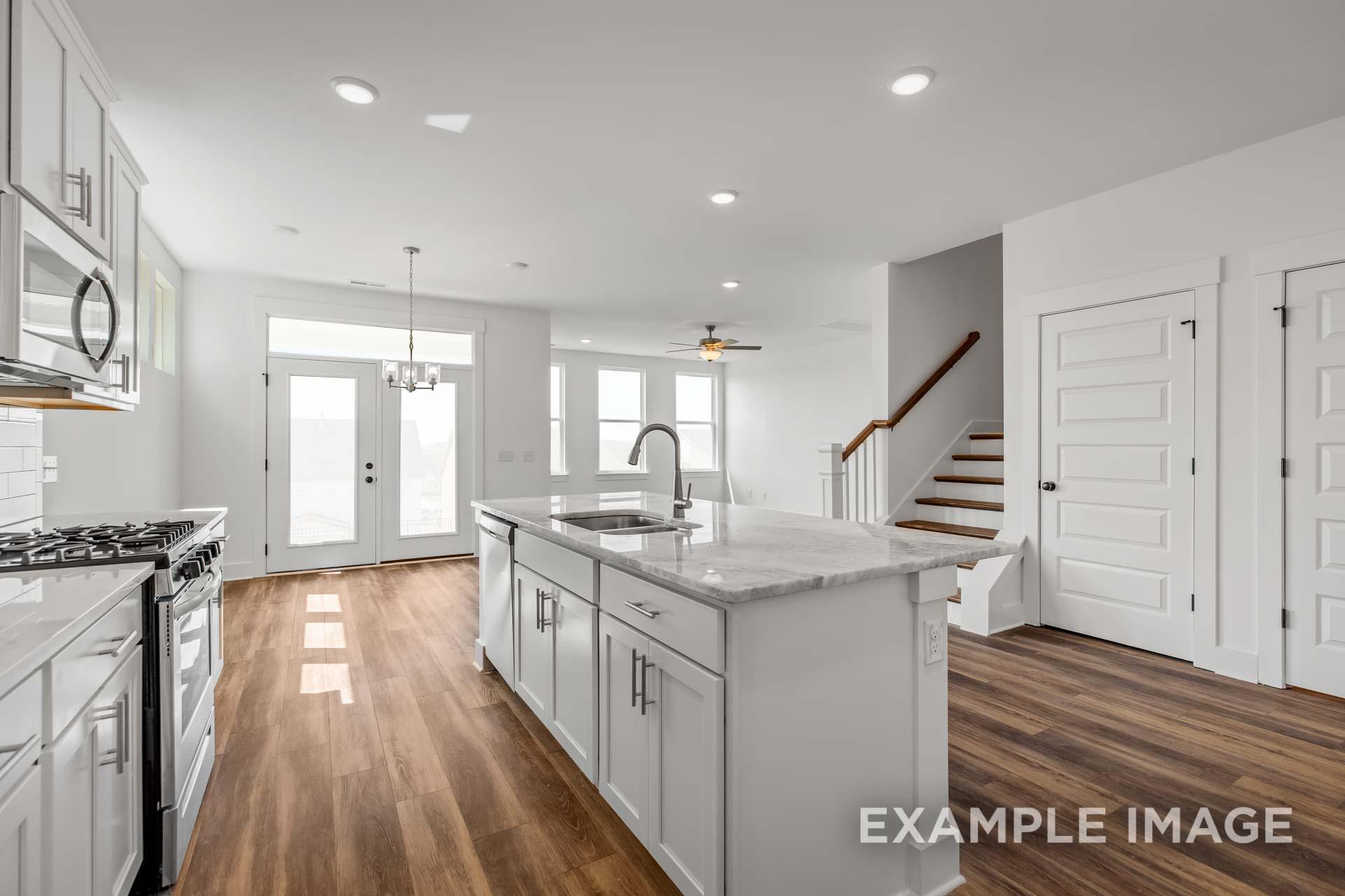 Open-concept kitchen in The Ash C with white shaker cabinets, marble island sink, gas range, and hardwood floors