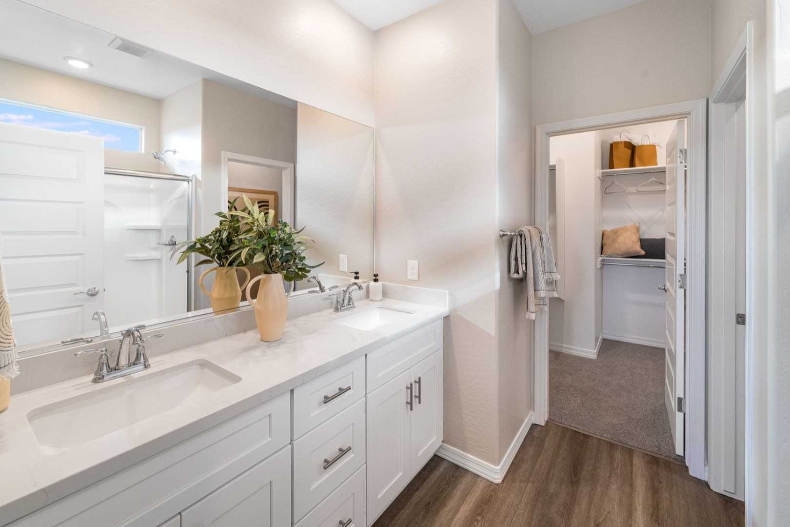 Spacious master bathroom in The Newport B with white double vanity, large mirror, potted plants, and walk-in closet