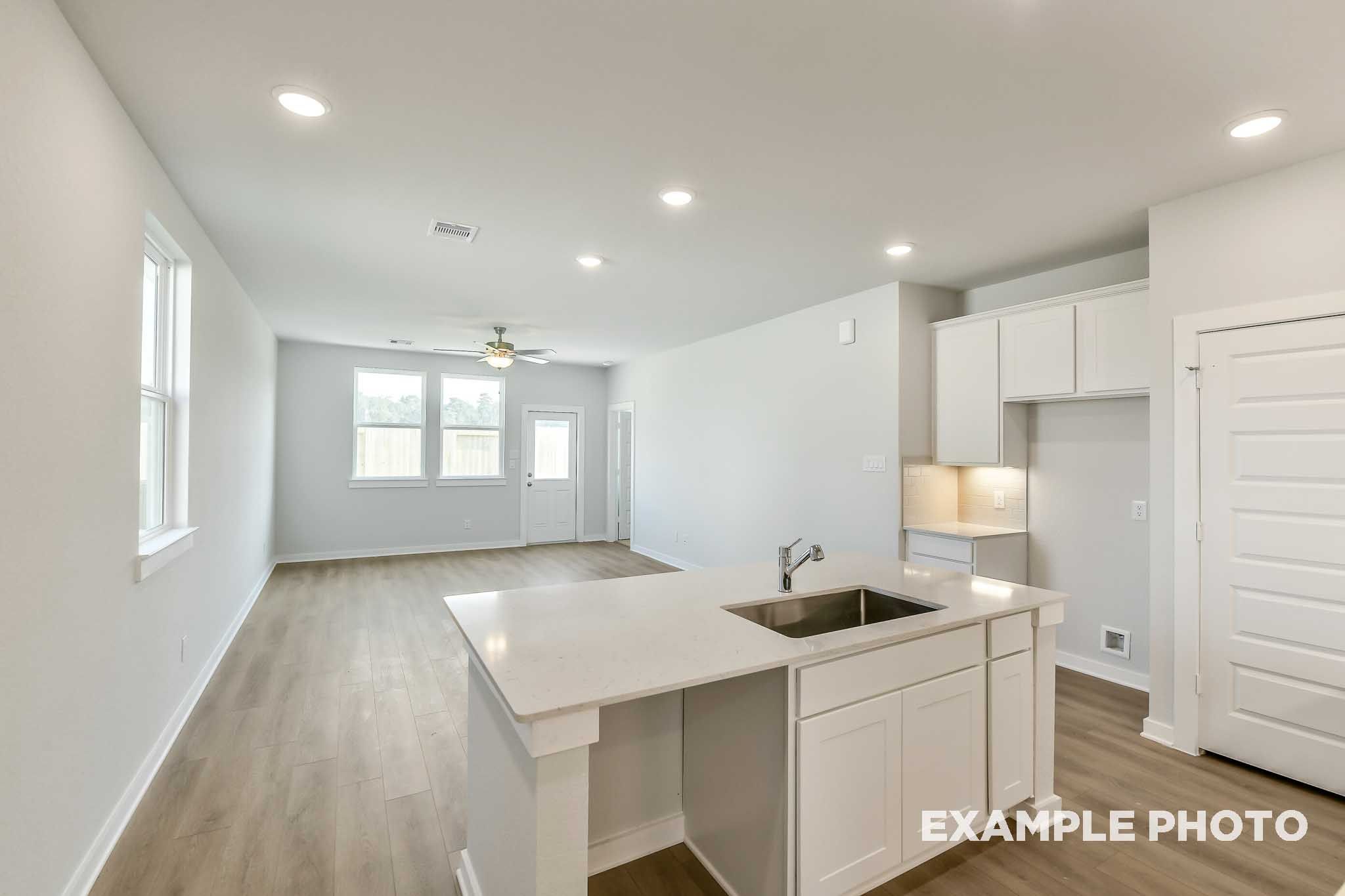 Open-concept kitchen and living area in The Colorado by Davidson Homes, featuring white cabinetry, island with sink, and wood-look flooring.