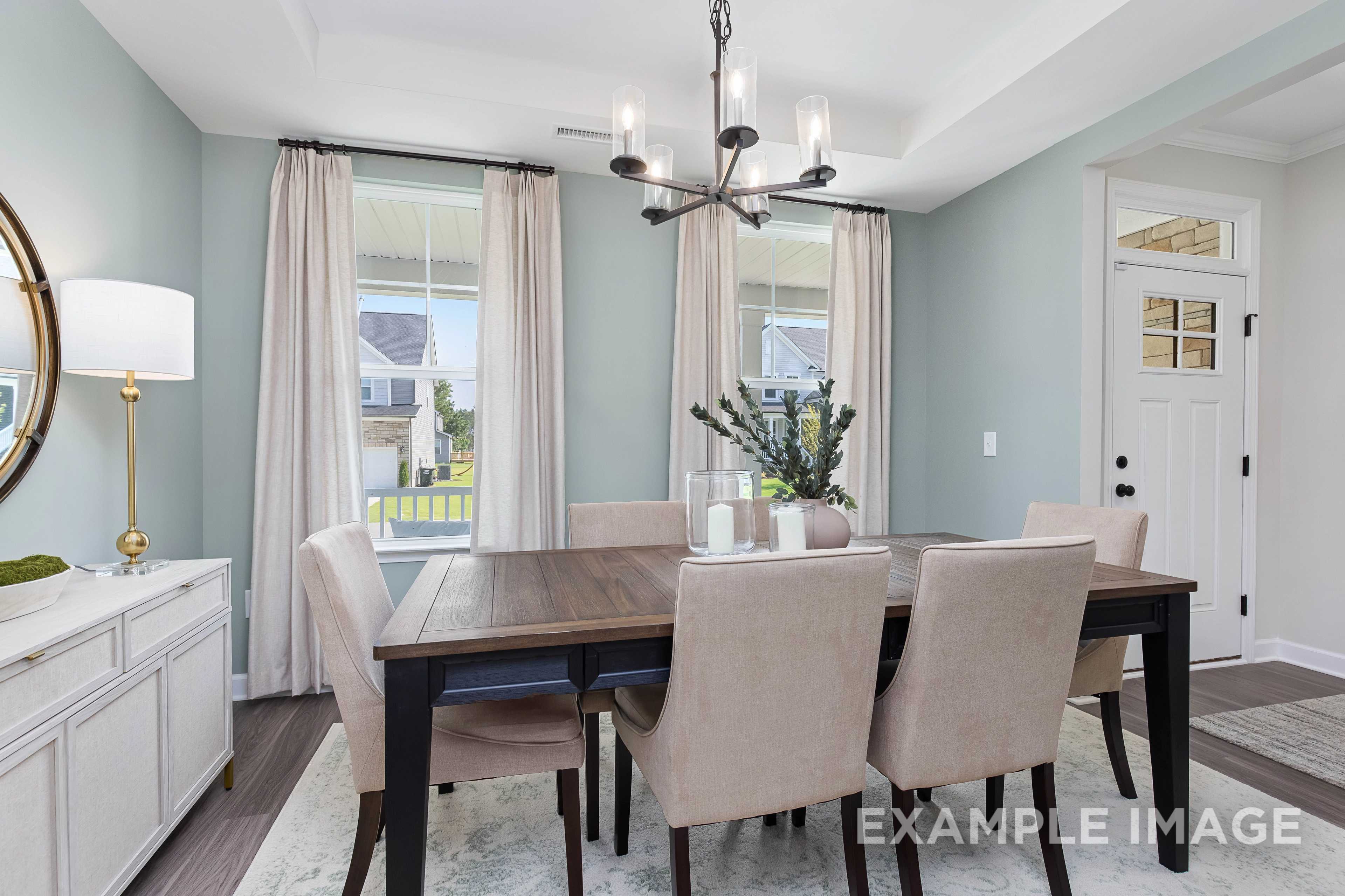 Spacious dining room in The Willow B with wooden table, beige chairs, chandelier, large windows, and soft blue walls