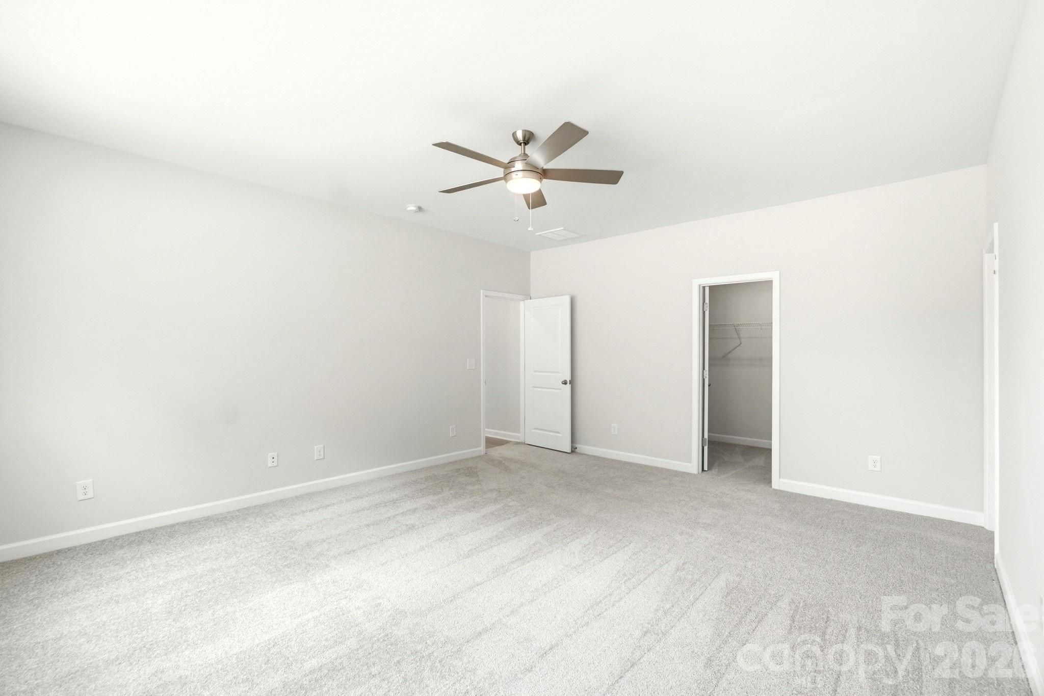 Spacious bedroom with plush carpeting, ceiling fan, and walk-in closet in The Magnolia B floor plan, Windgate, Mooresville.