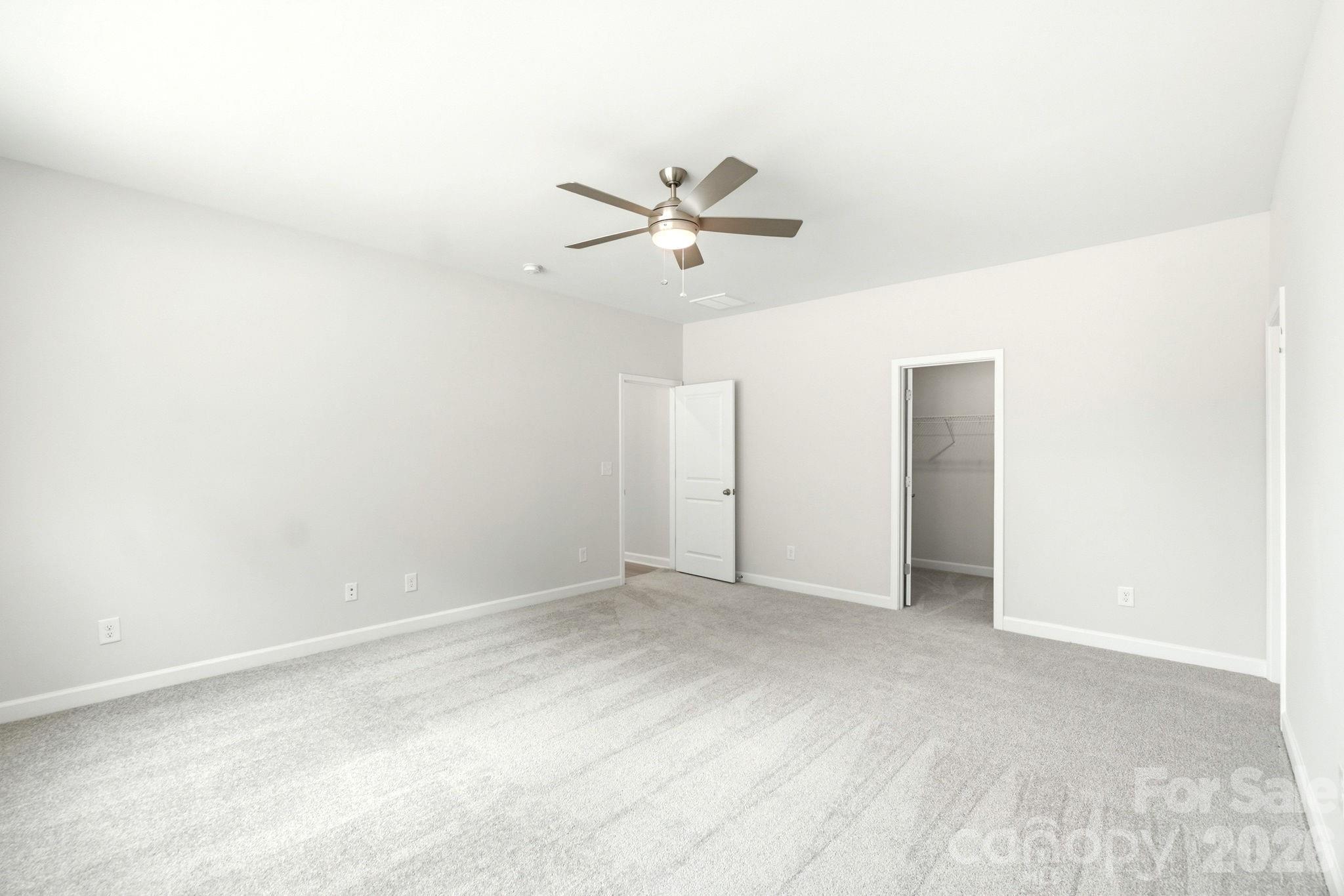 Spacious bedroom with plush carpeting, ceiling fan, and walk-in closet in The Magnolia B floor plan, Windgate, Mooresville.