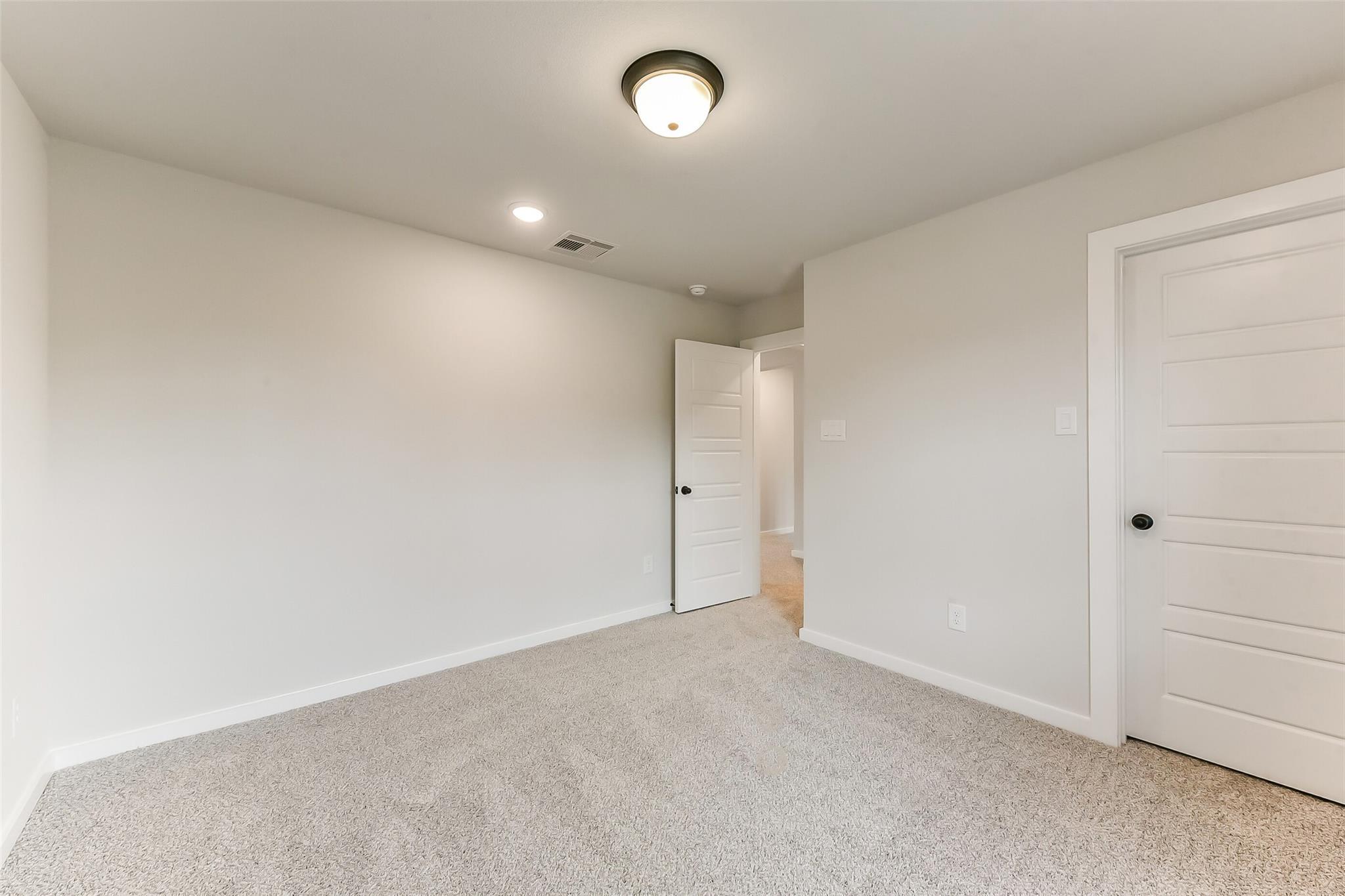 Empty bedroom with beige walls, neutral carpet, open door to adjoining bath in Davidson Homes The Sequoia C, Sundance Cove, Crosby Texas