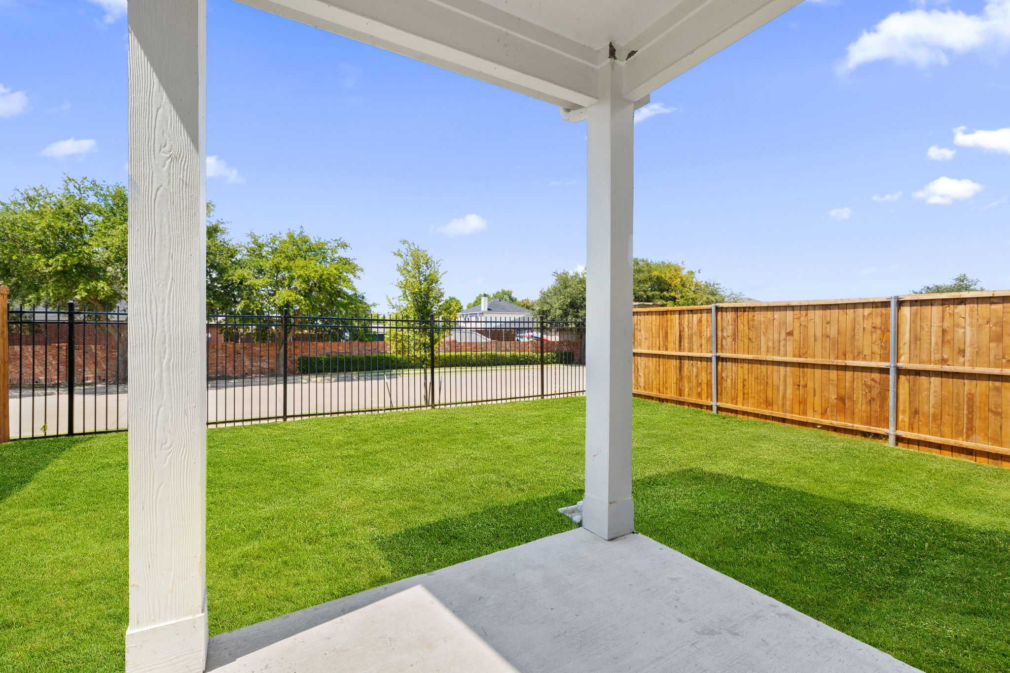 Covered back patio with white columns overlooking lush green backyard and wooden fence in Davidson Homes The Durham E, Wylie, Texas
