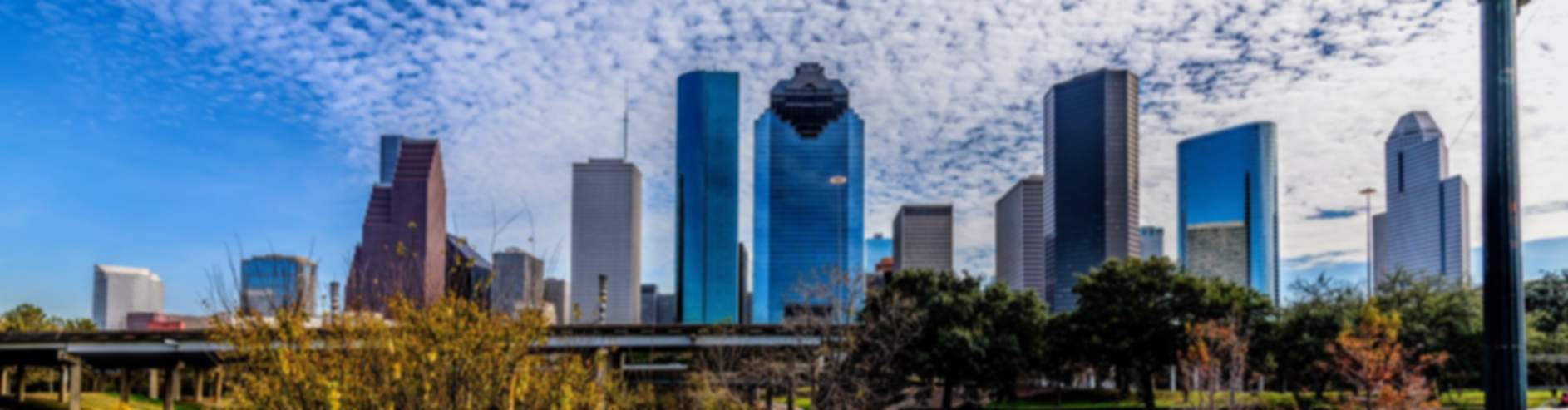 Houston skyline with modern skyscrapers, stone bridge over bayou, autumn foliage, and lamp post in Houston Region