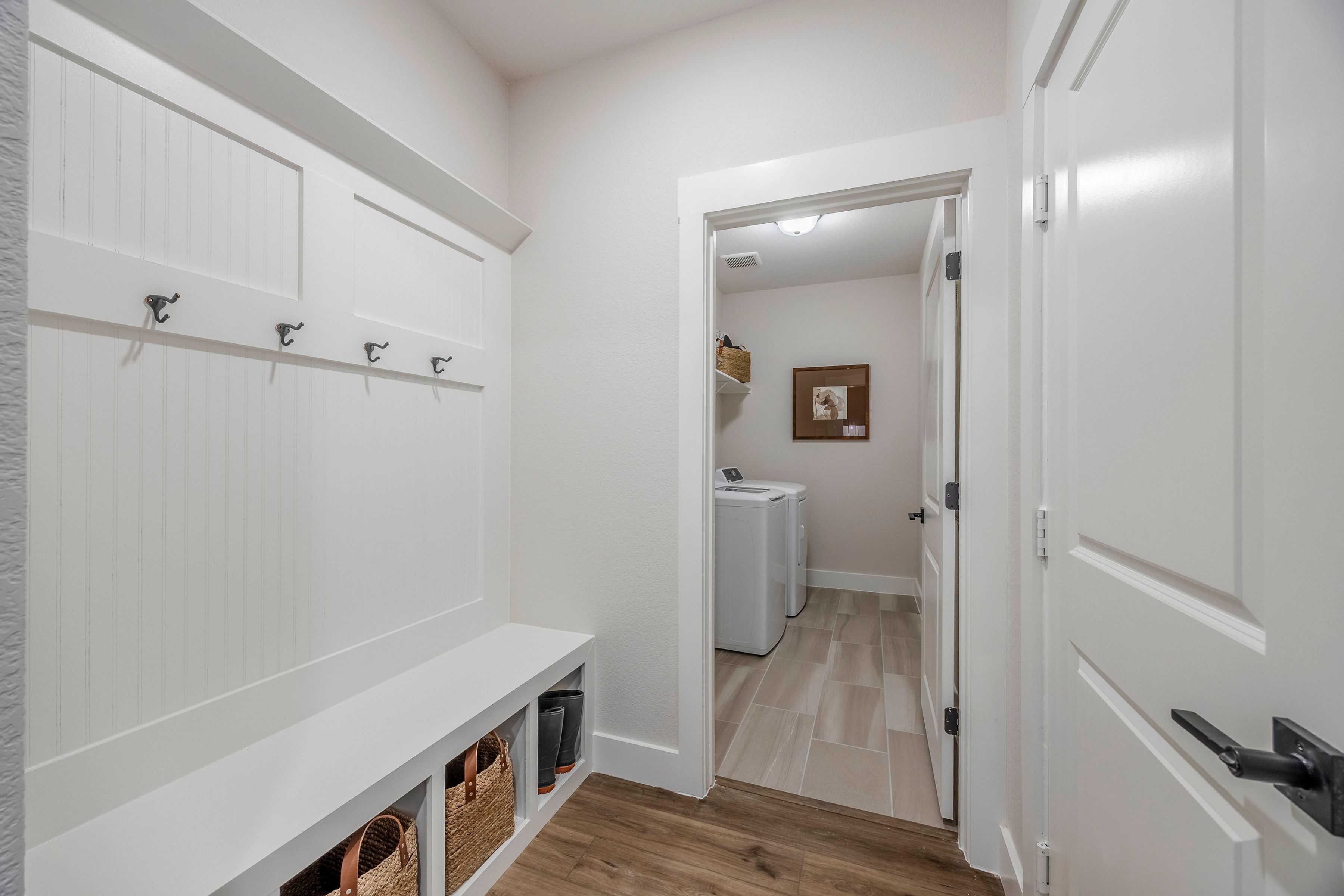 Spacious mudroom in The Rockford home with white shiplap walls, built-in bench, hooks, baskets, and laundry nook
