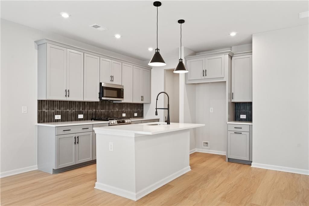 Modern kitchen featuring gray shaker cabinets, white quartz island, stainless appliances, black pendant lights in Davidson Homes The Marion A, Kennesaw, GA