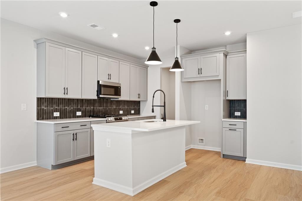 Modern white kitchen island with stainless appliances, black pendant lights in Davidson Homes The Marion A, Kennesaw, GA